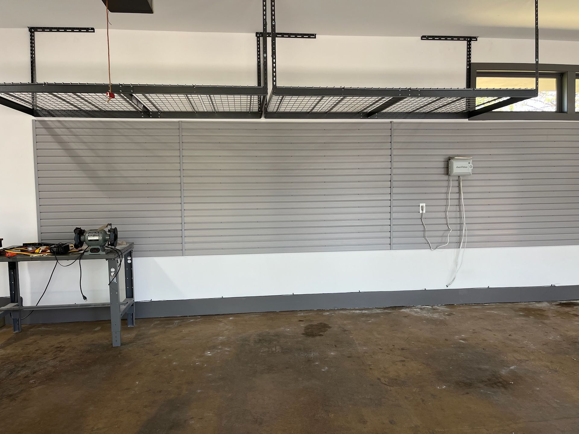 Garage interior with gray slat wall, workbench, and concrete floor under overhead storage racks