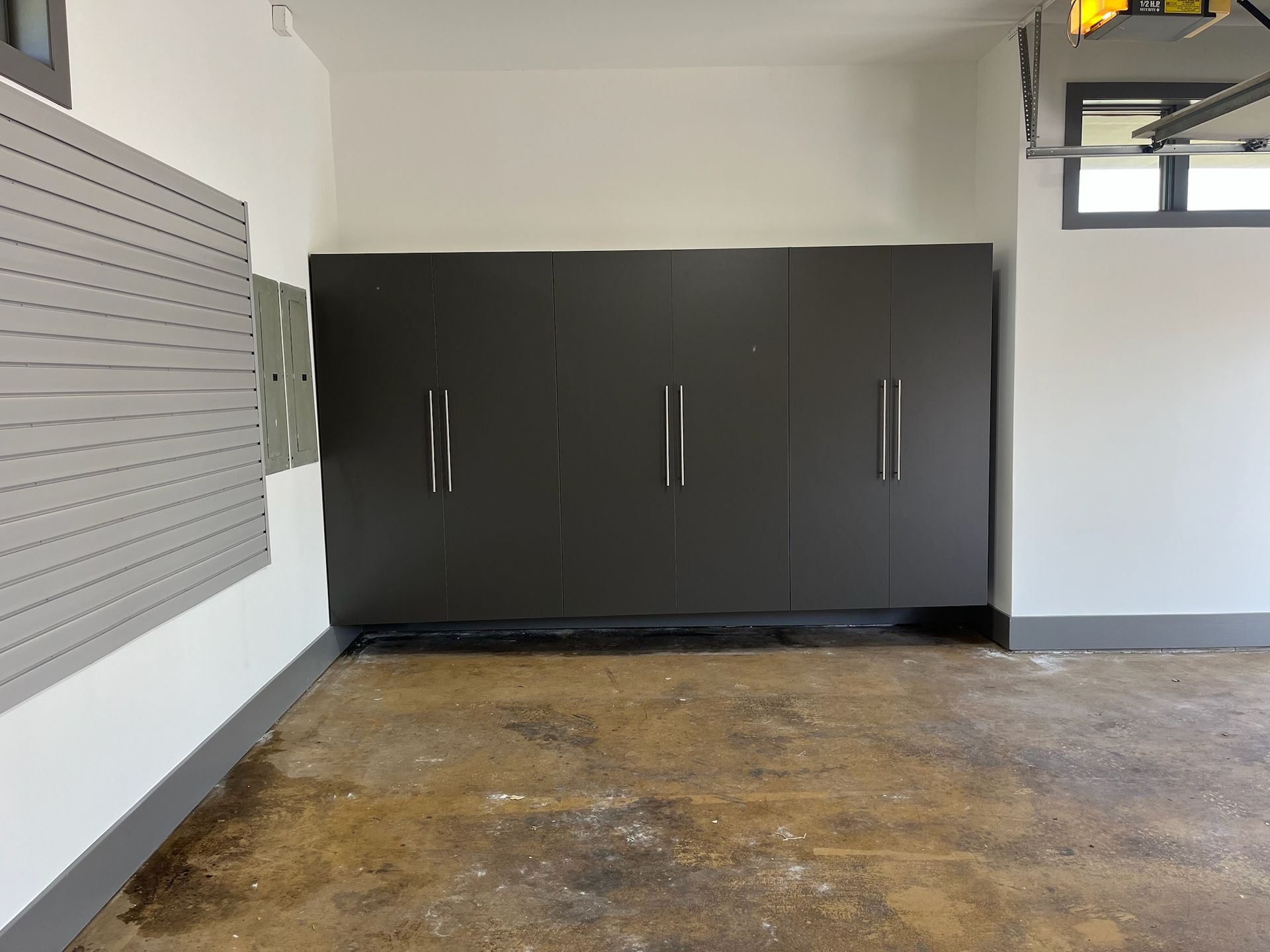 Empty garage with dark storage cabinets, gray walls, and a worn concrete floor