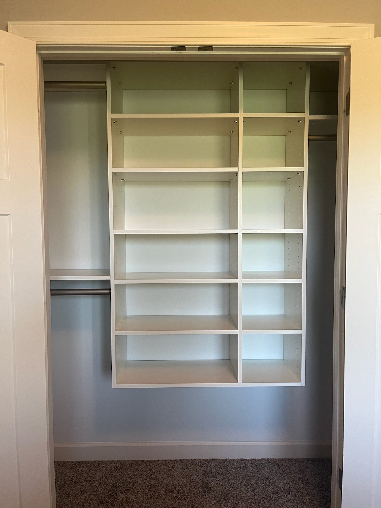 Empty white closet shelving with hanging rod and built-in drawers in a beige room
