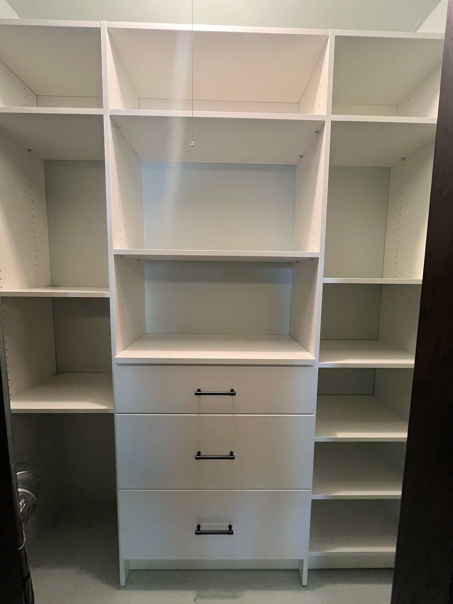 White built-in closet with shelves, hanging rods, and three drawers against a light wall