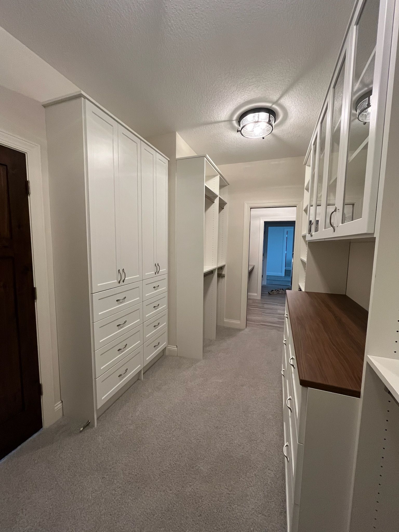Narrow hallway with white cabinets, carpeted floor, and a blue-lit room at the far end.