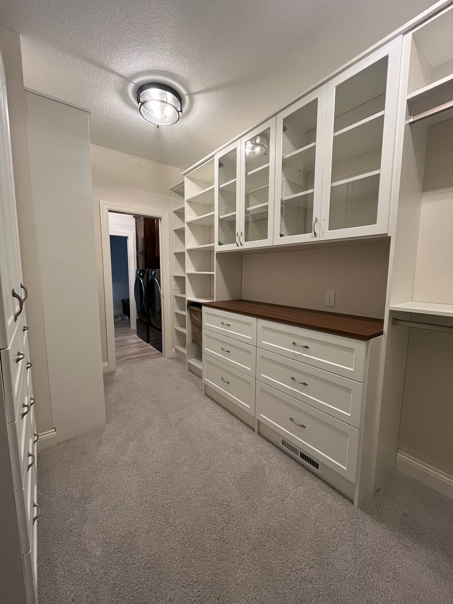 Bright walk-in closet with white cabinets, glass-front upper shelves, and carpeted floor.