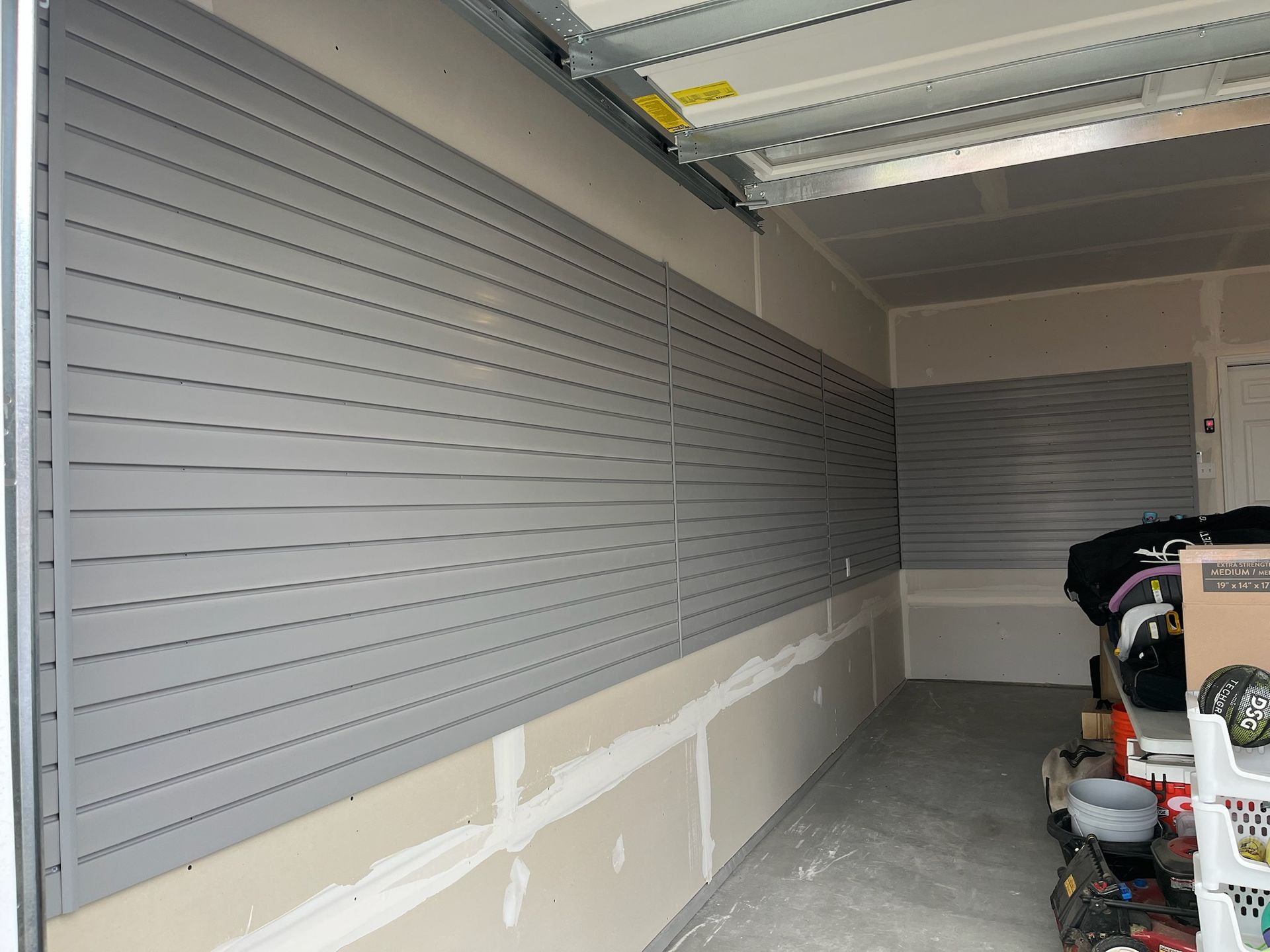 Empty garage with gray slatwall panels and unfinished lower walls under a raised garage door.
