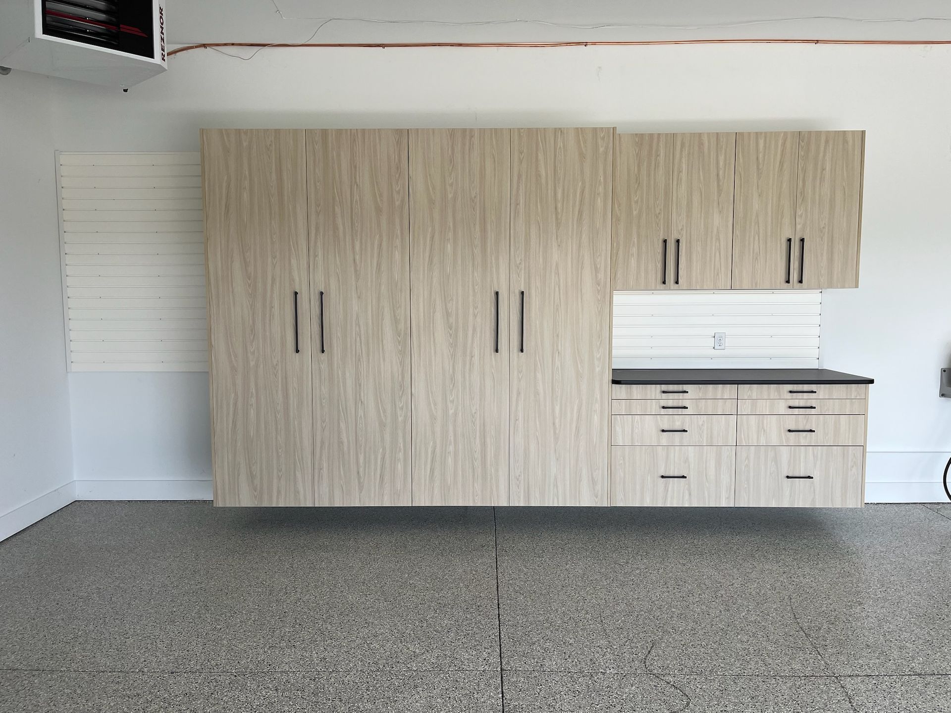 Large beige storage cabinets and countertop in an empty garage with speckled flooring.