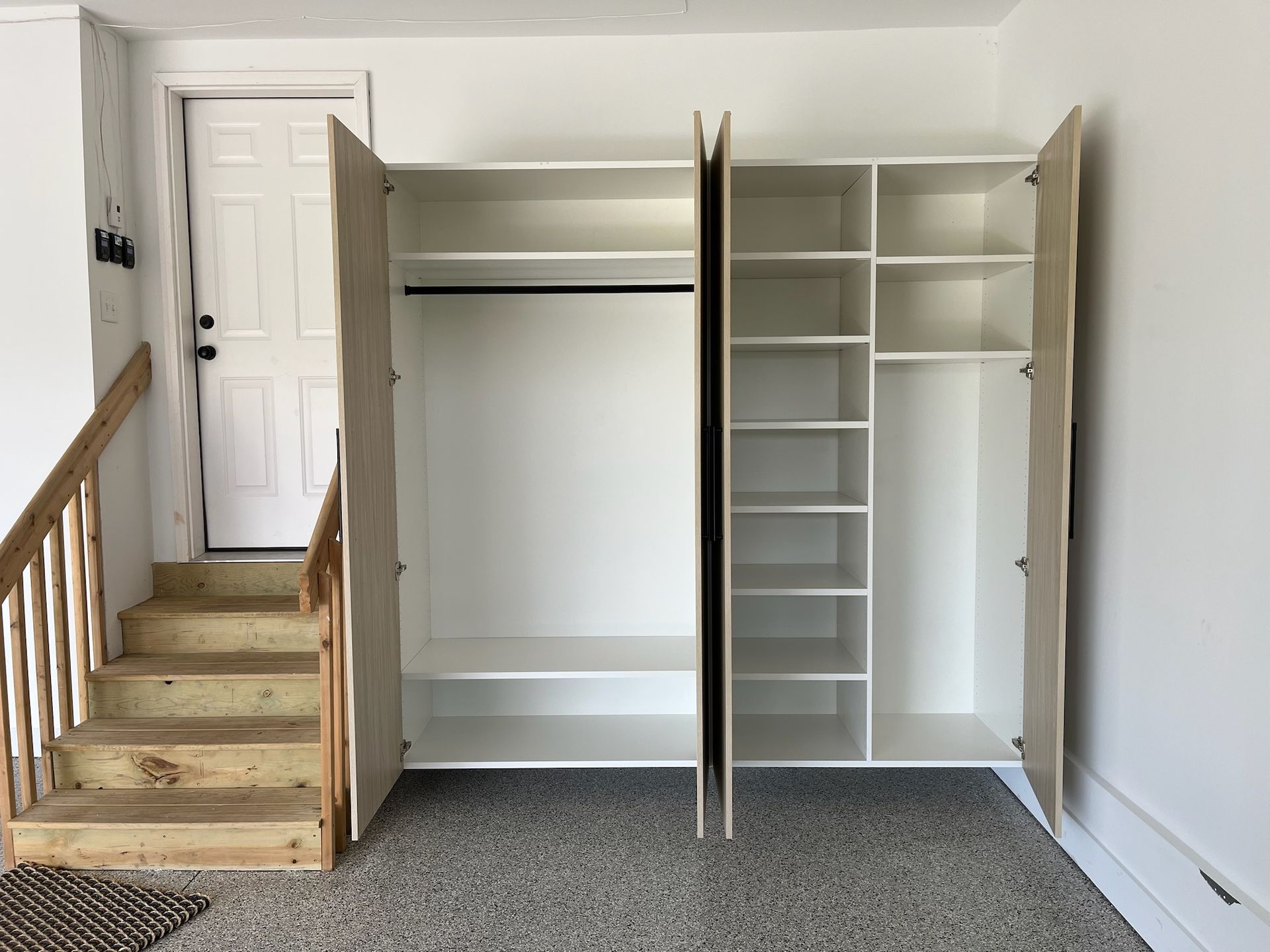 Built-in white closet with open doors beside a carpeted stairway in a bright room
