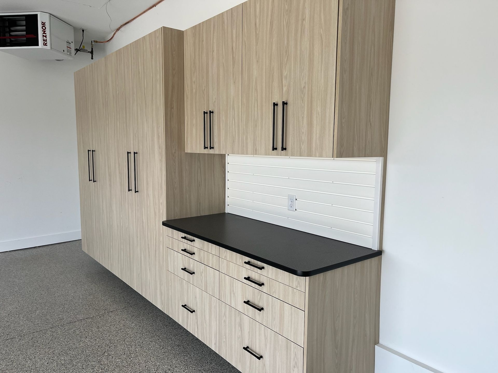 Built-in wood cabinets with black countertop and white tile backsplash in a utility room