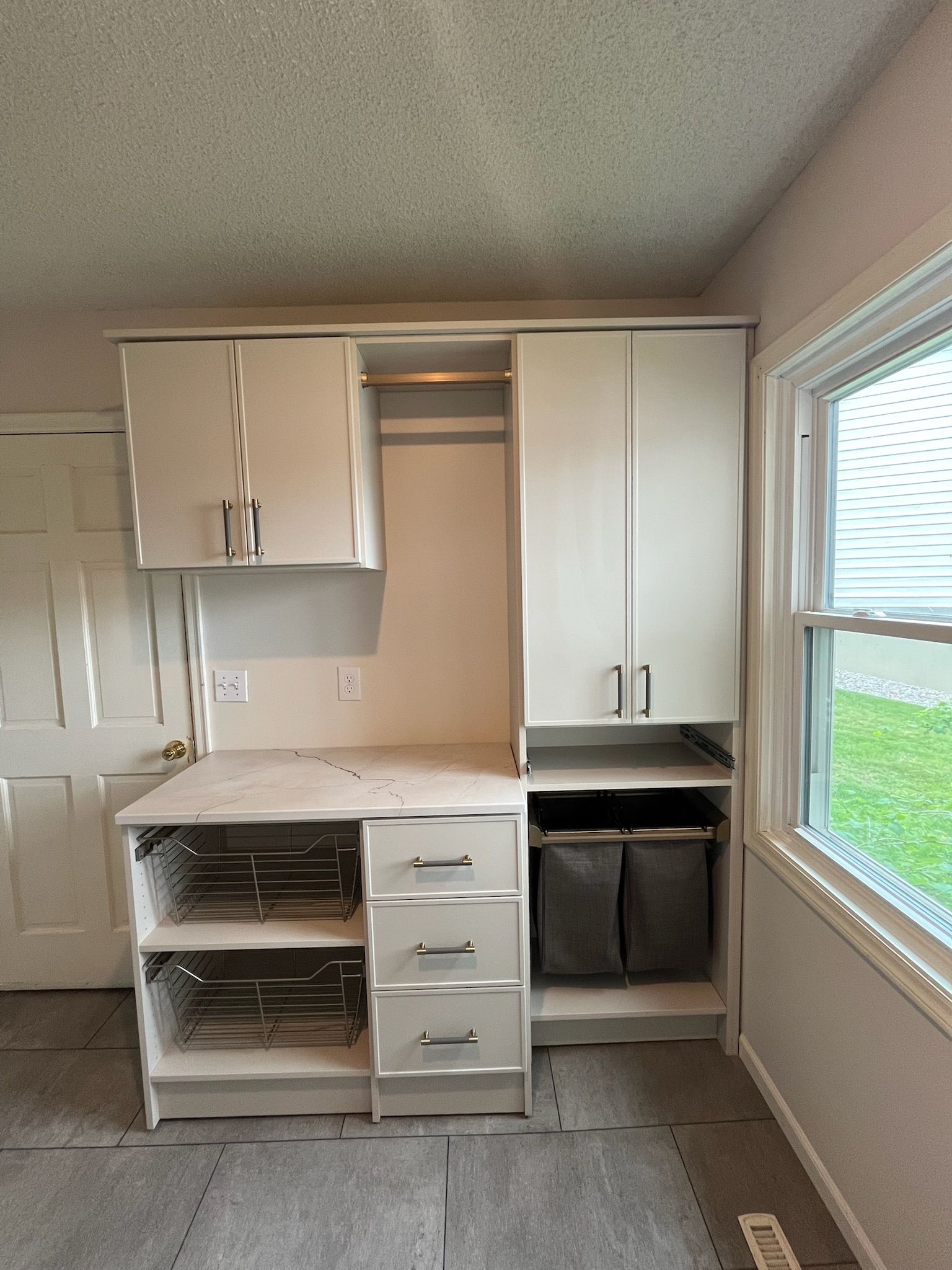Small kitchen with white cabinets, open drawers, and a window overlooking grass.