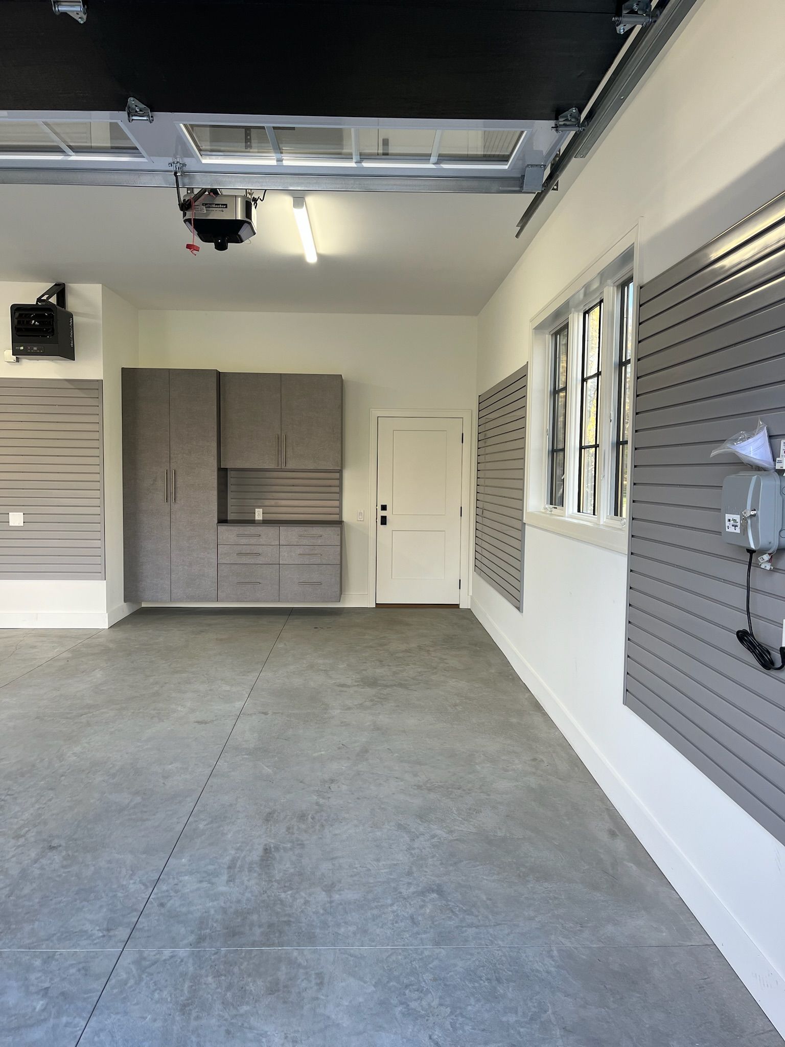 Empty garage interior with gray cabinets, windows, and a raised roll-up door opener overhead