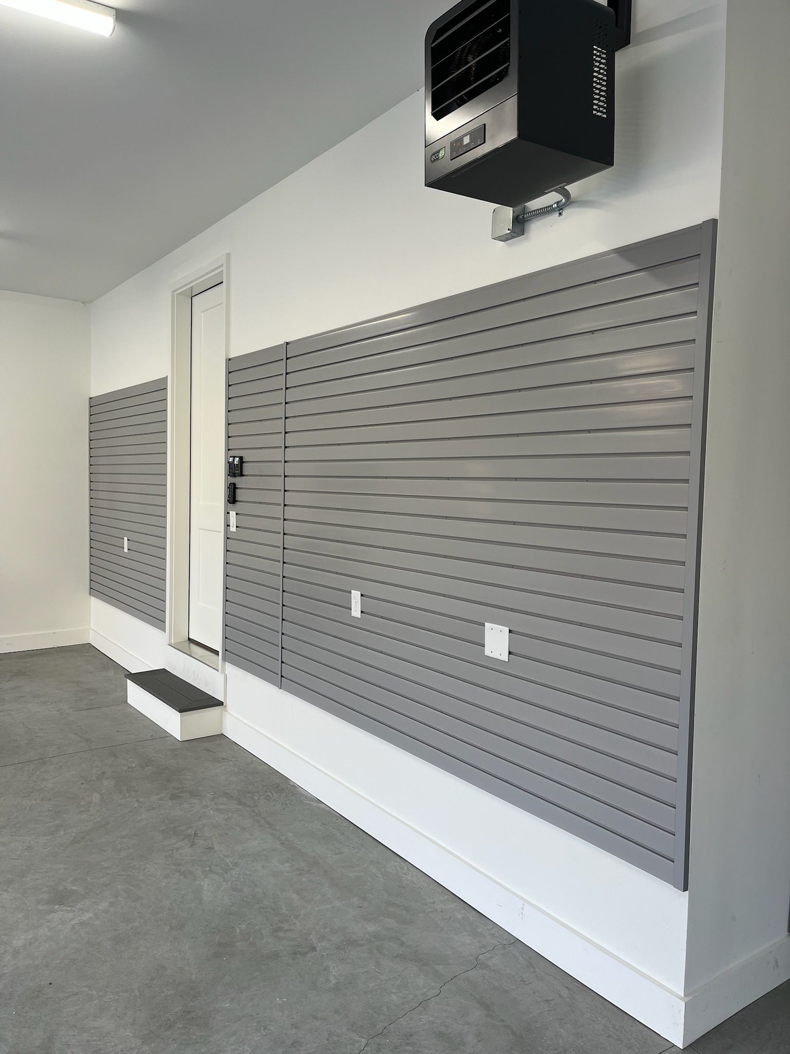 Interior of a store with gray slatwall display panels, white walls, and a ceiling-mounted heater.