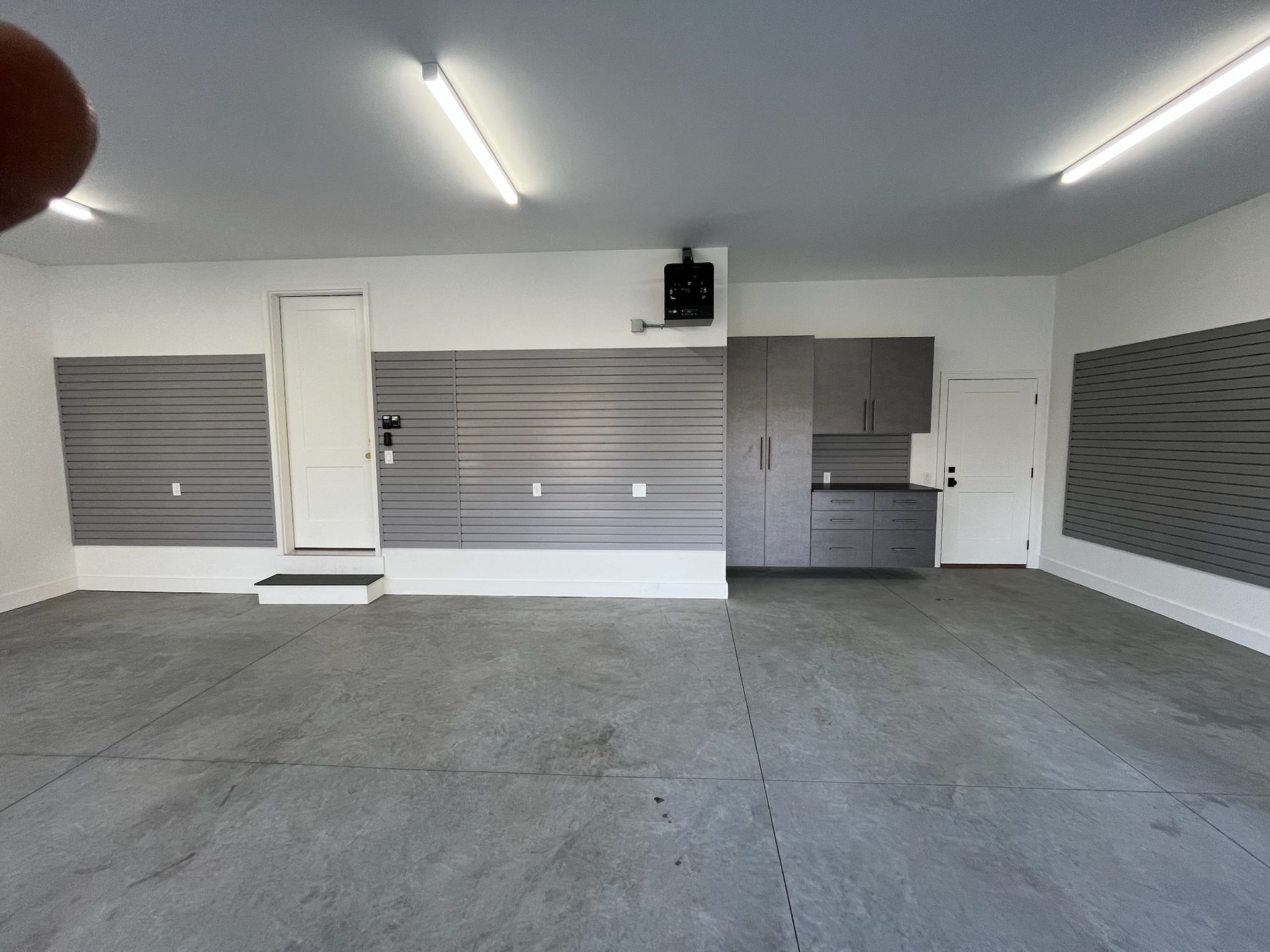 Empty gray garage interior with closed roll-up doors and fluorescent ceiling lights