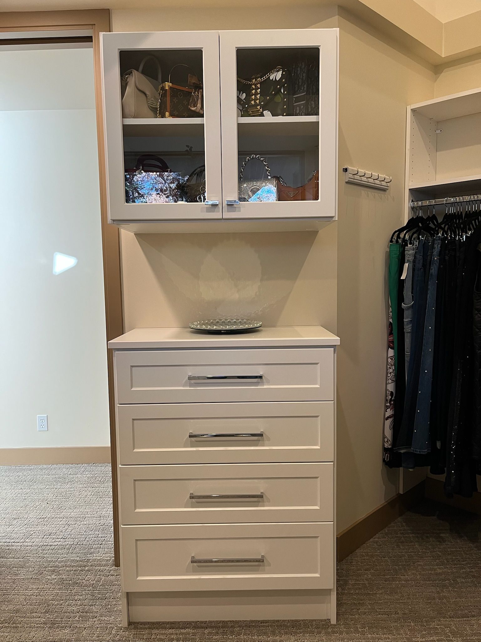 White bedroom closet unit with upper cabinets and a four-drawer dresser beneath a decorative bowl.