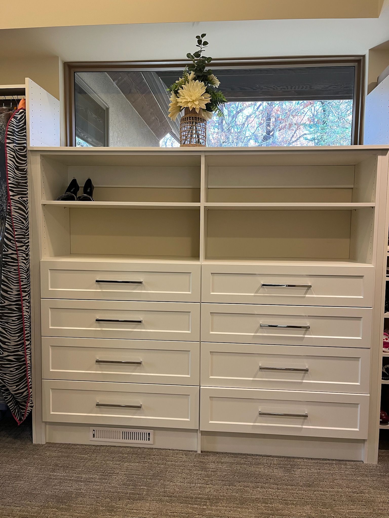 White dresser with open shelves under a window, decorated with a hanging plant.