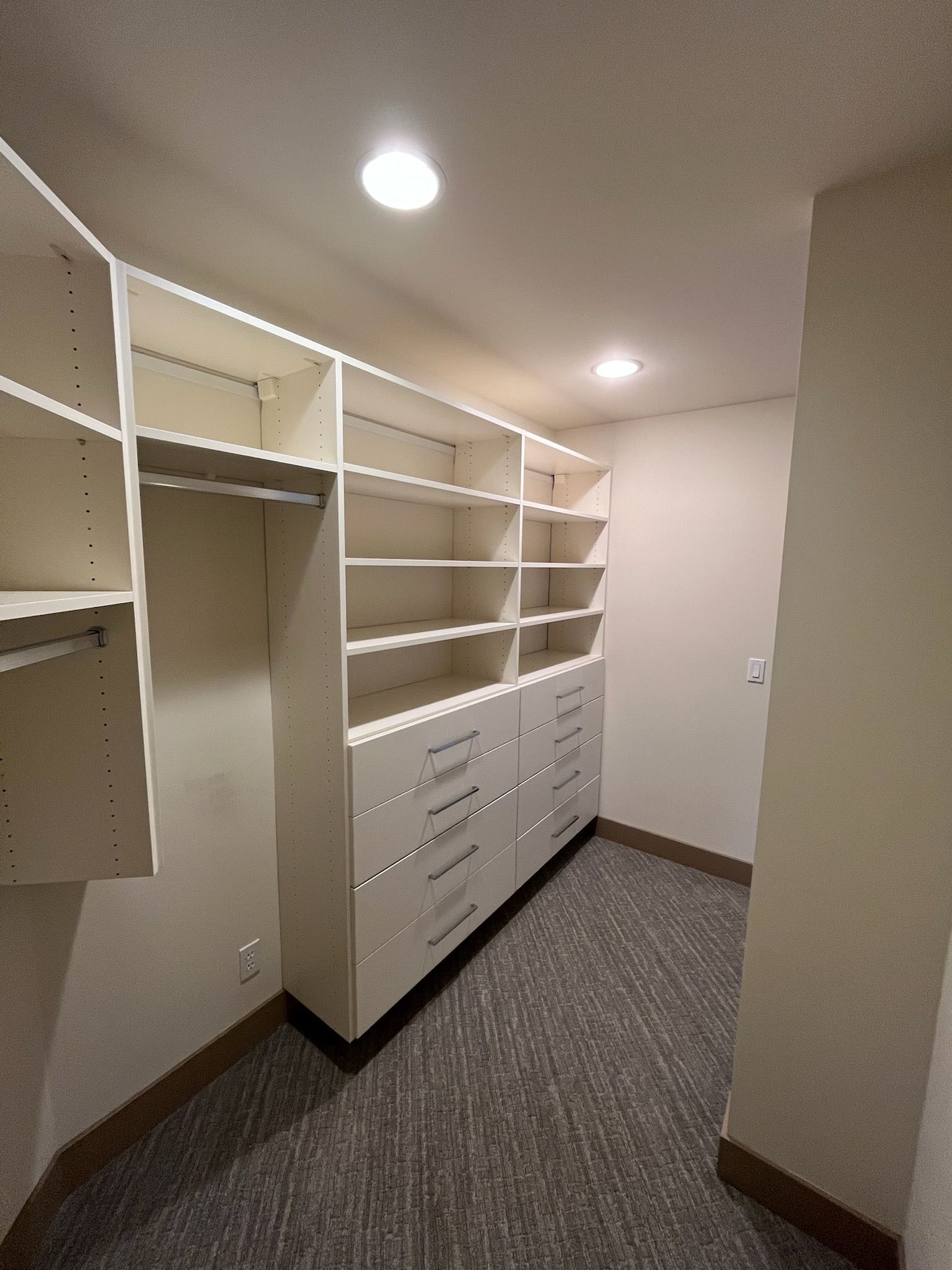 Built-in white shelving and drawers in a narrow closet or dressing room with carpeted floor.