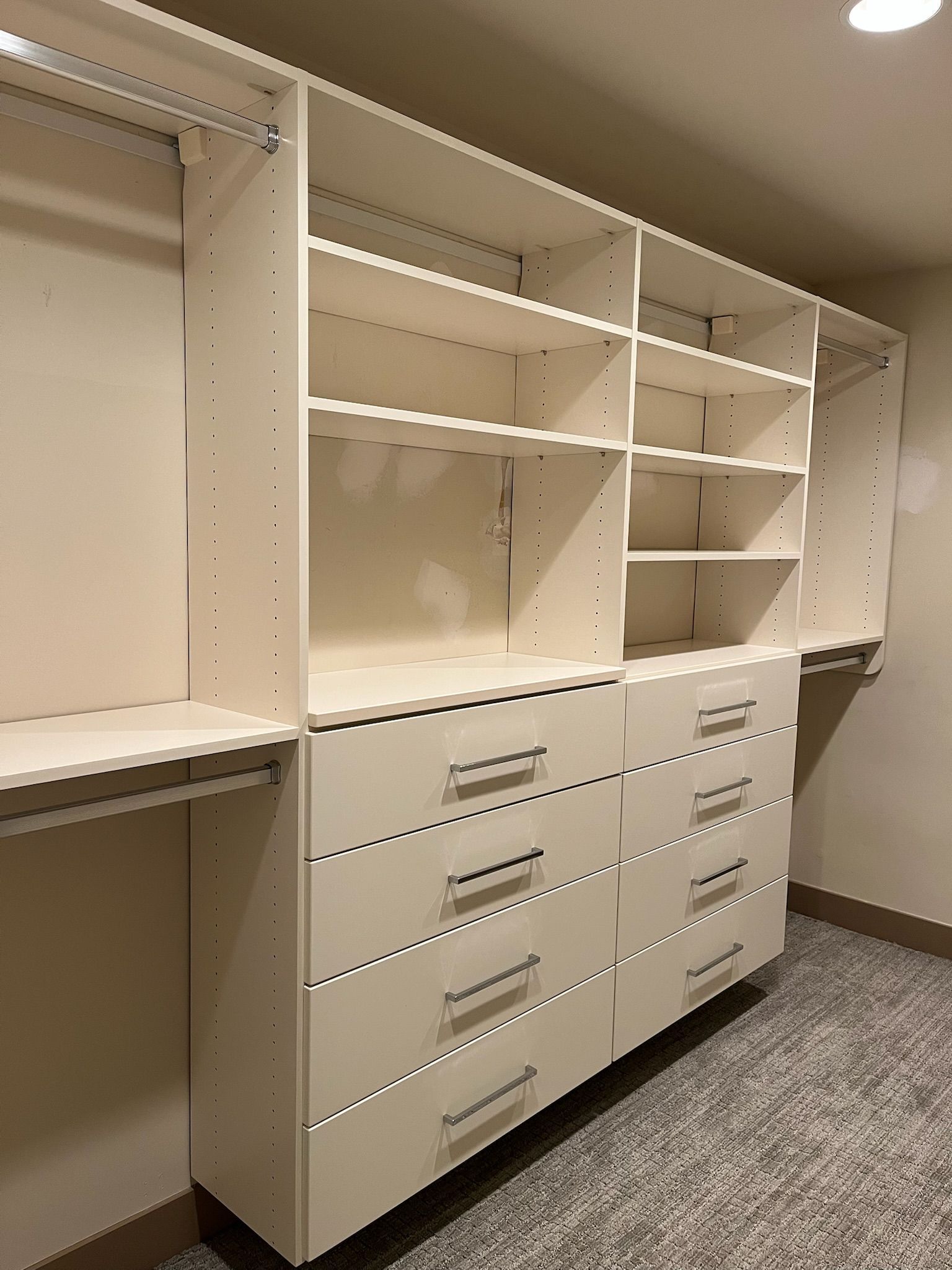 Built-in white closet organizer with shelves and drawers in a hallway or dressing room.