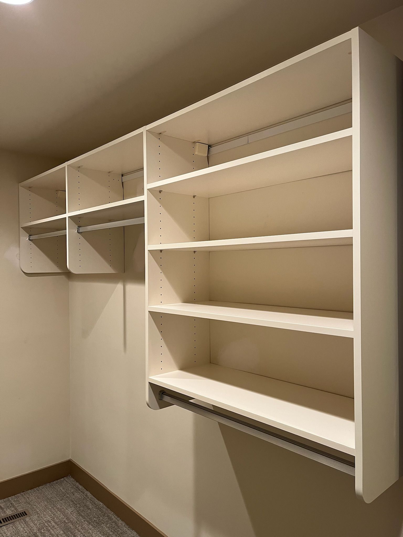 Empty beige wall-mounted shelving unit in a closet or pantry, with multiple compartments and one pull-down shelf.