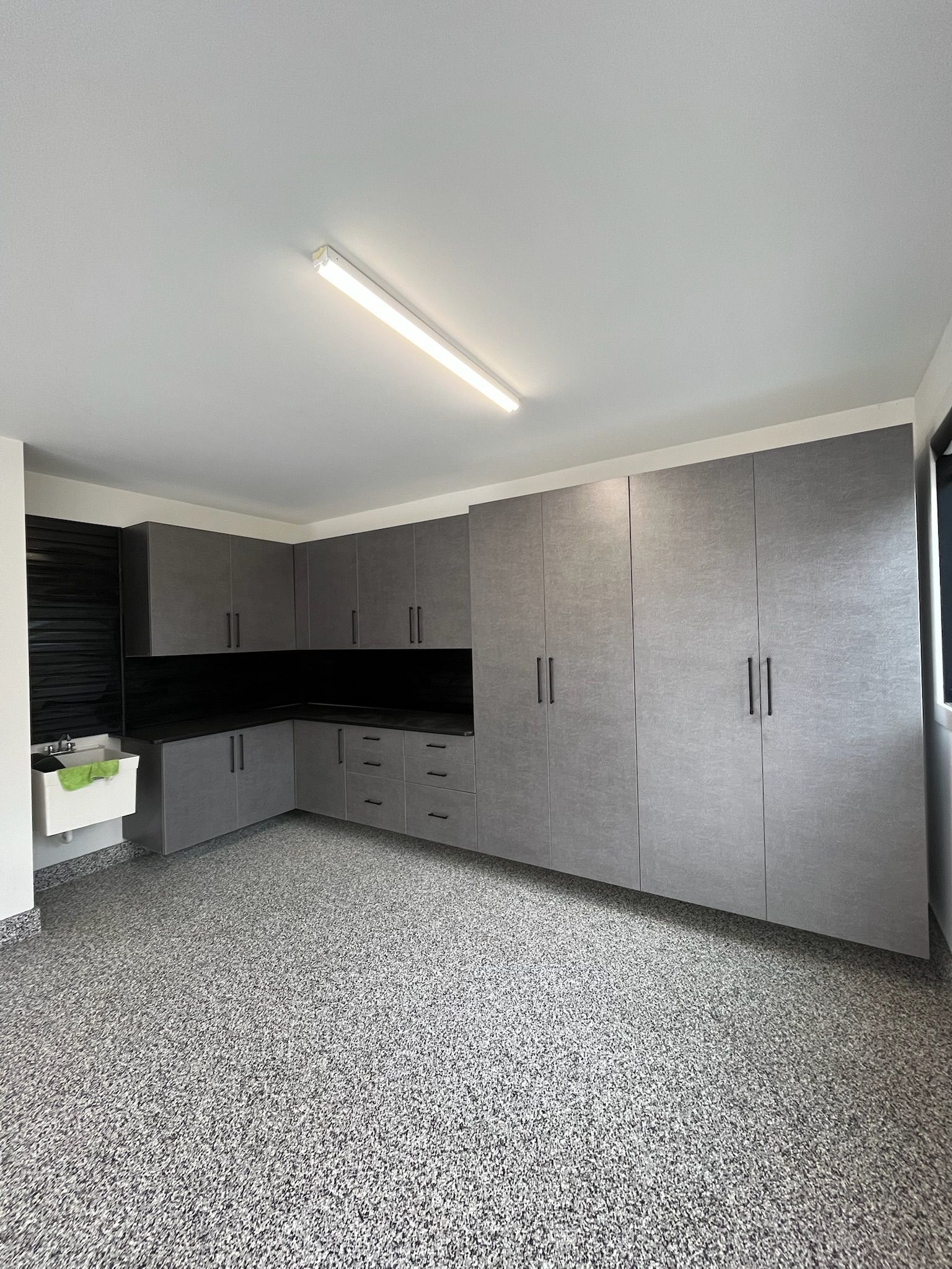 Empty modern kitchen with gray cabinets, black countertops, and speckled flooring.