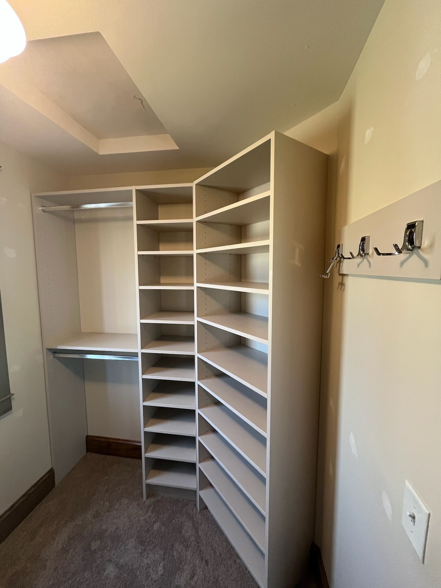 Empty closet with white built-in shelving, hanging rods, and beige walls.