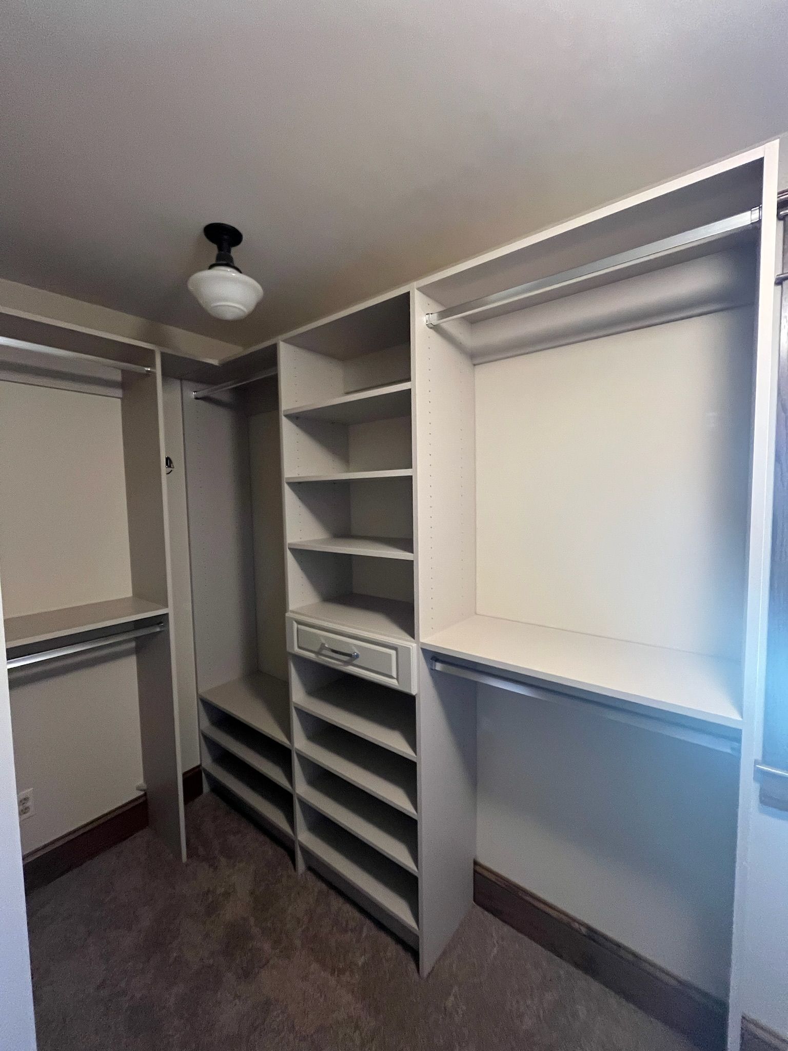 Walk-in closet with white shelving, hanging rods, and shoe racks, lit by a ceiling light.
