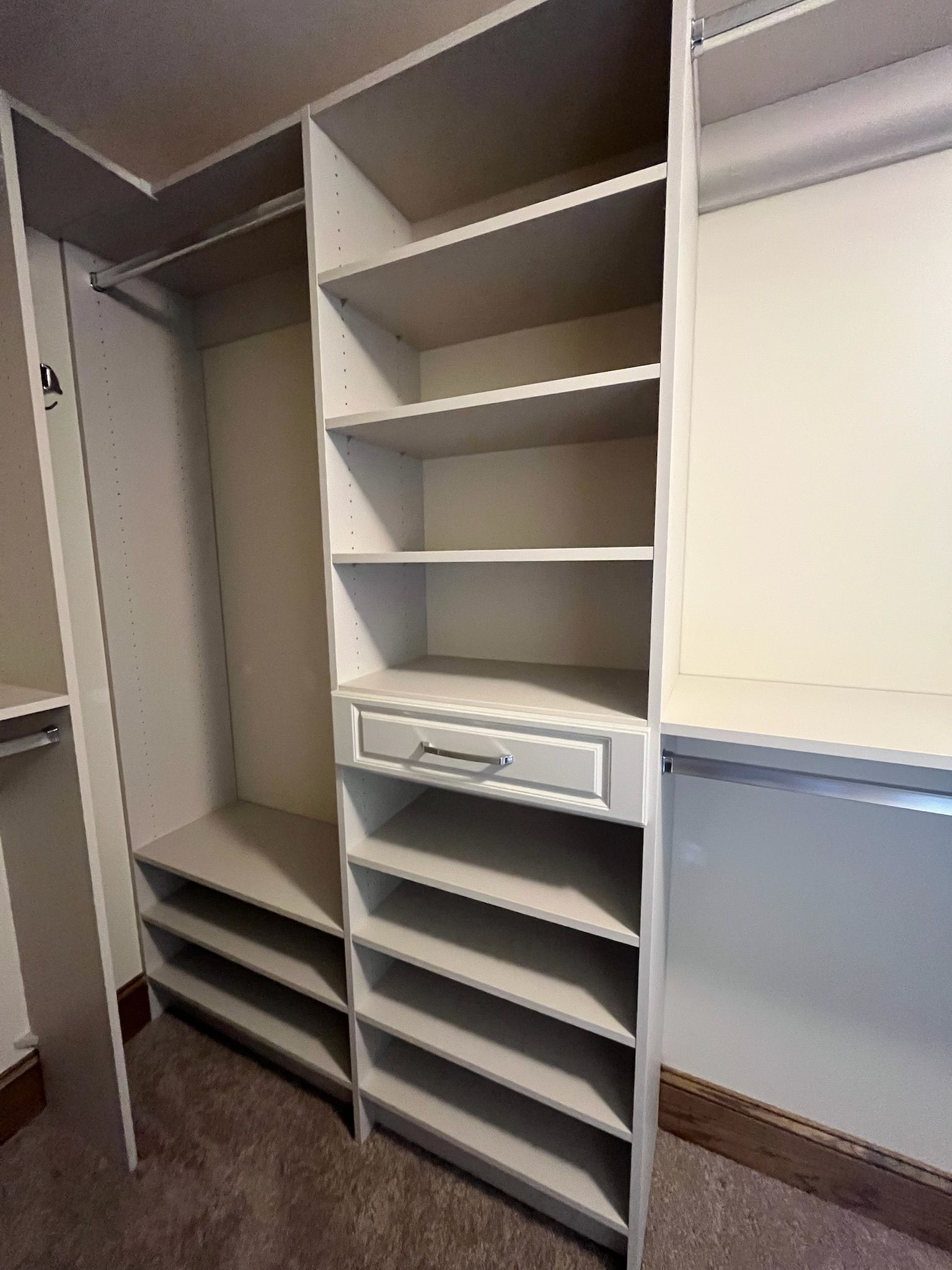 Open closet with white shelving, hanging rod, drawers, and empty compartments on a carpeted floor.