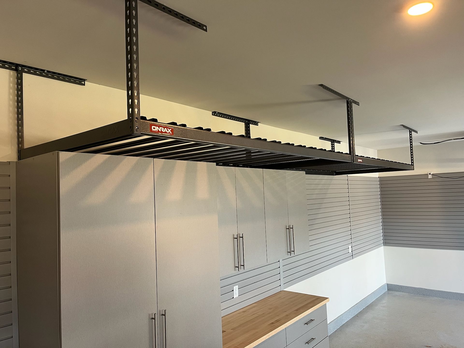 Garage with white cabinets, slatted wall panels, wood countertop, and overhead storage racks