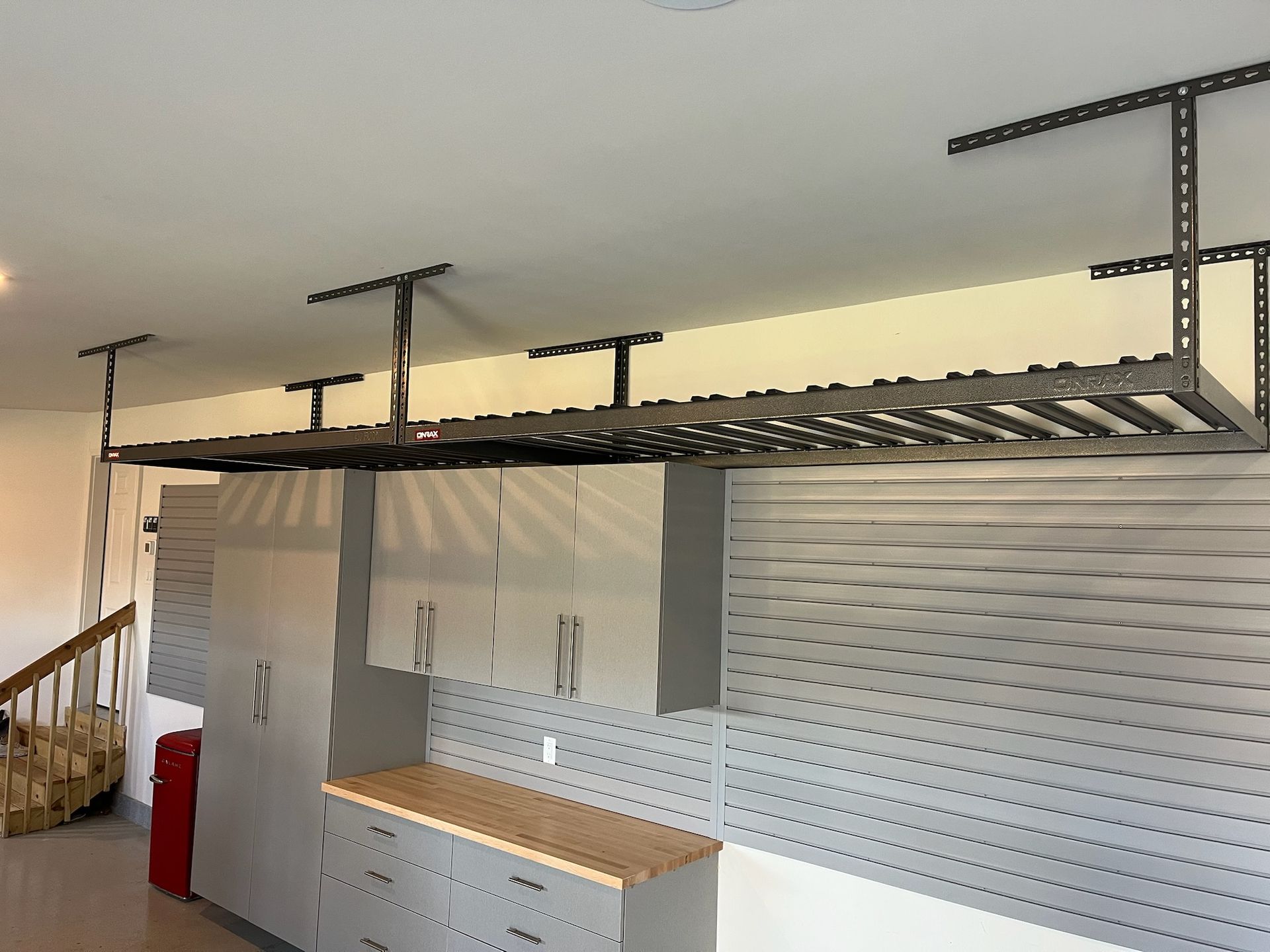 Large overhead metal storage rack mounted above a garage/workshop wall with cabinets and a countertop below