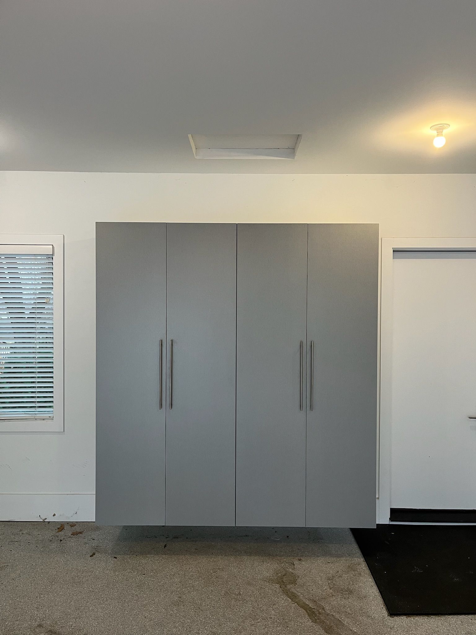 Gray storage cabinet in a room with white walls, windows, and a black mat on the floor.