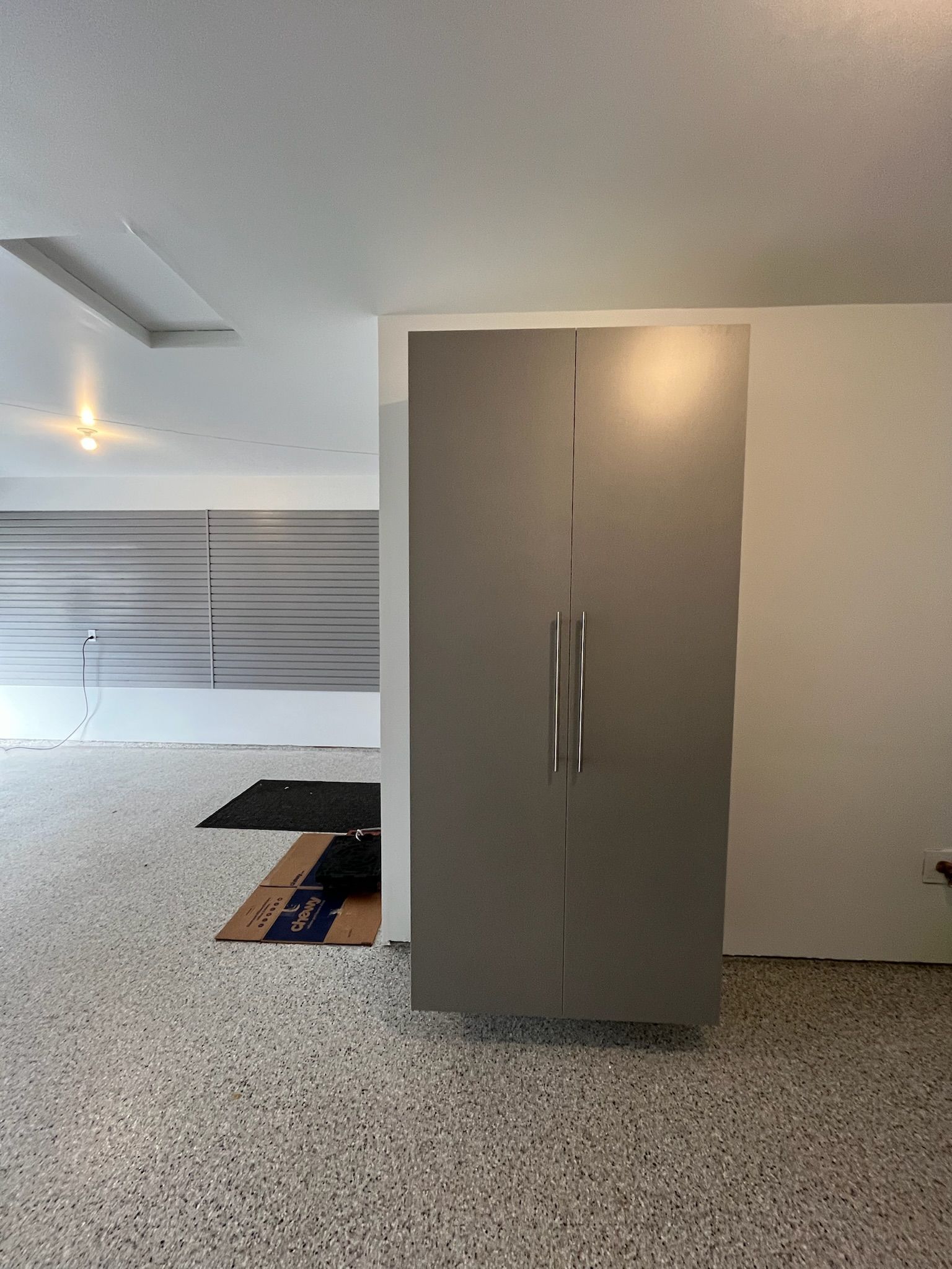 Modern kitchen with speckled floor, gray cabinet, and an open floor hatch near large windows.