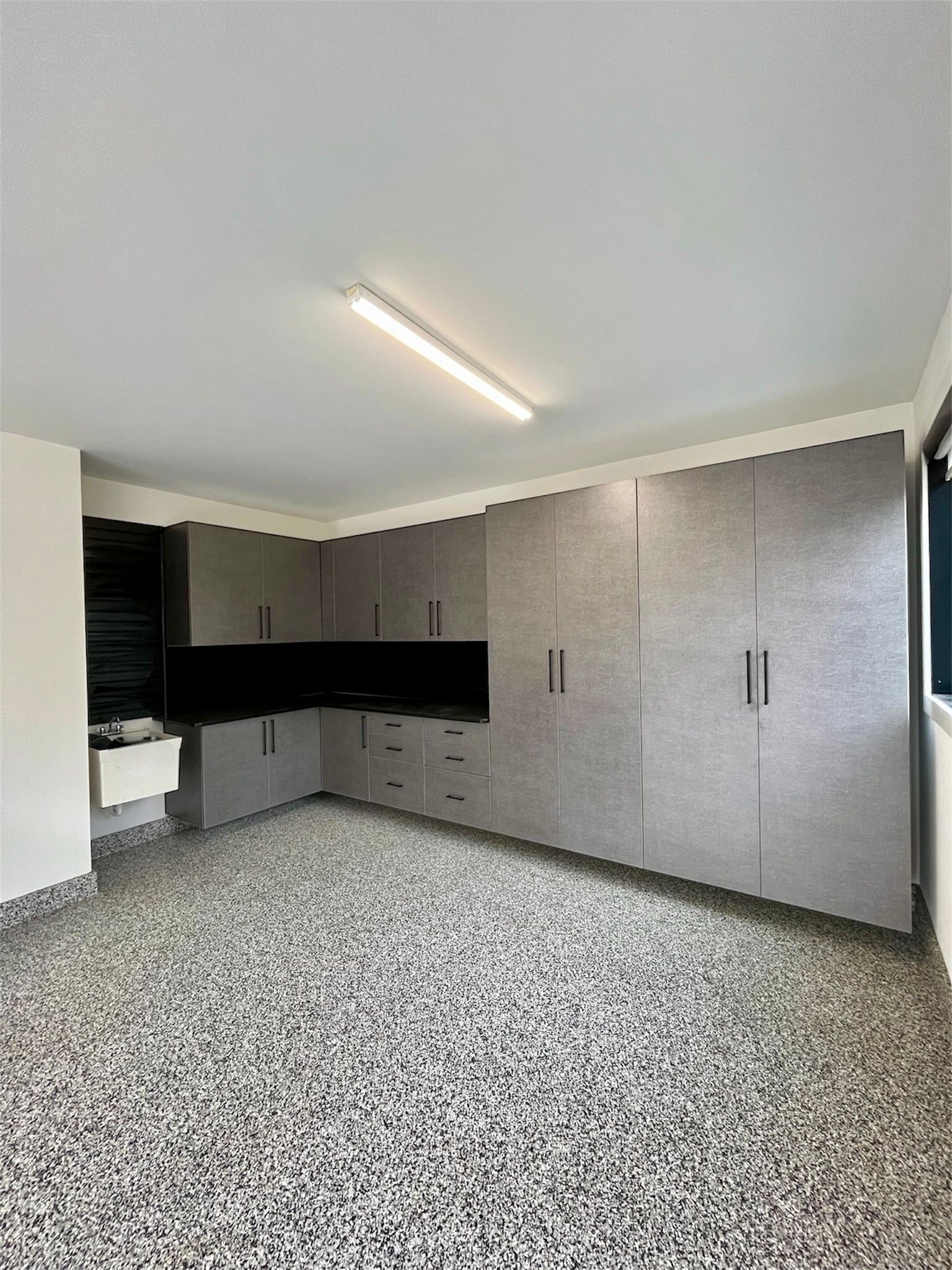 Empty modern room with gray cabinets, black countertop, and speckled tile floor under fluorescent light
