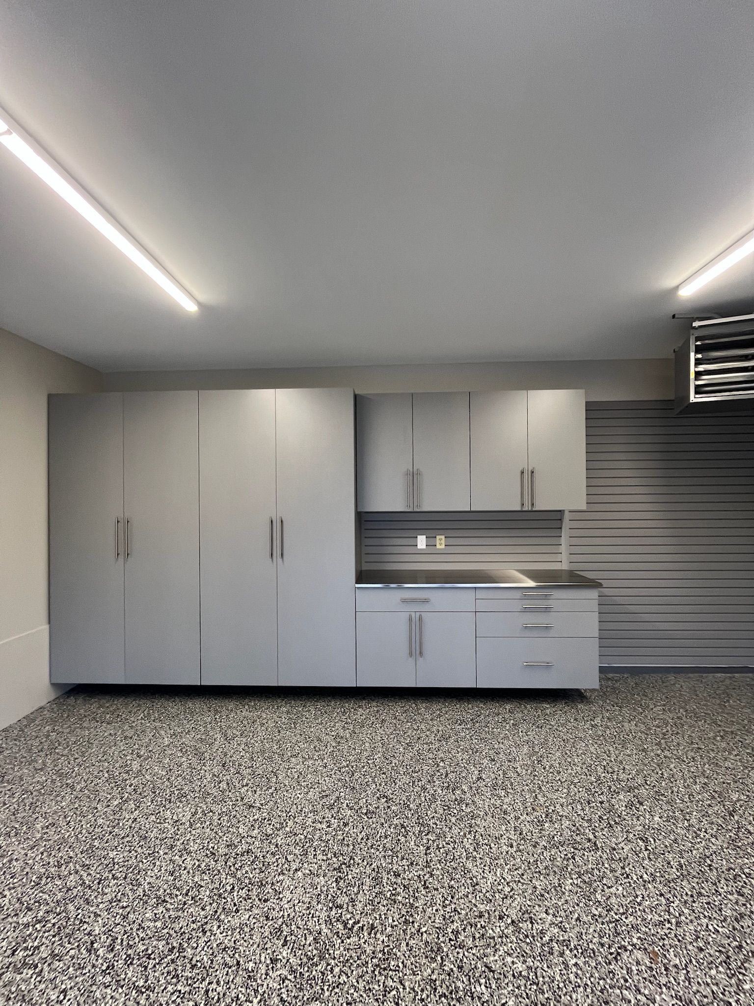 Modern garage with gray cabinets, countertop sink, and speckled epoxy floor under fluorescent lights