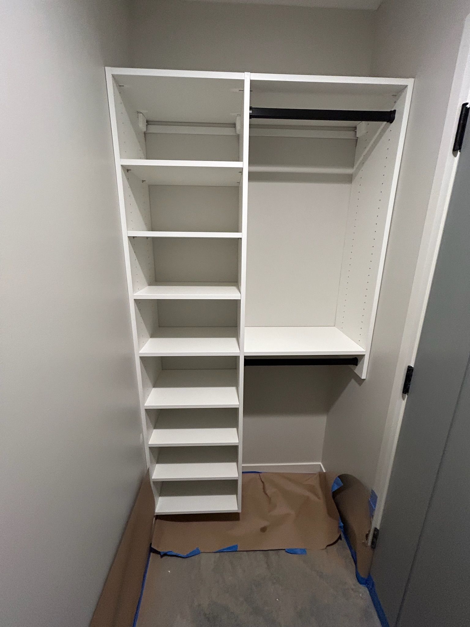 Empty white closet with shelves and hanging rod, cardboard on the floor, and a blue cable near the back wall