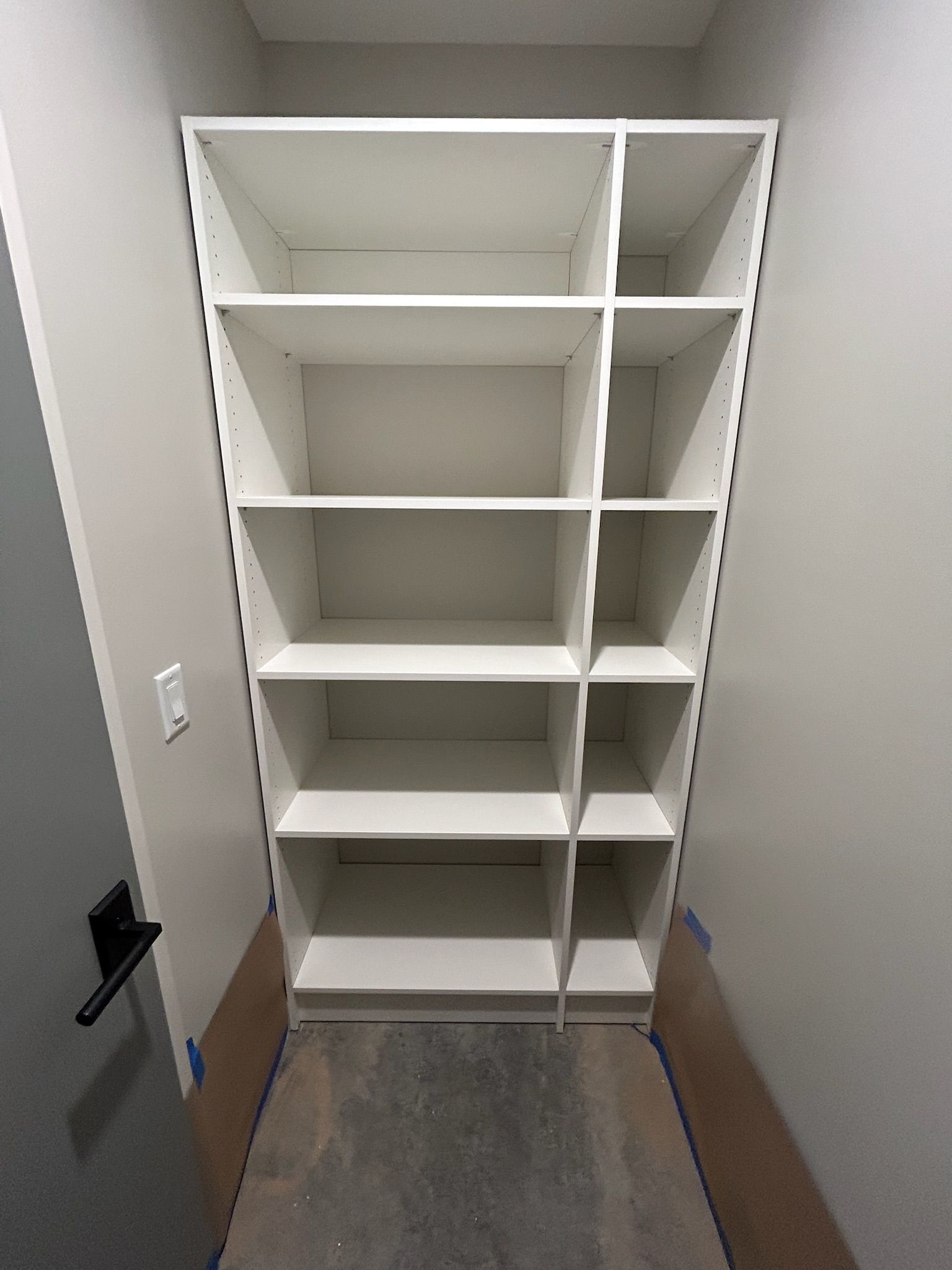 White built-in shelving unit in a small closet with gray carpet and beige walls.
