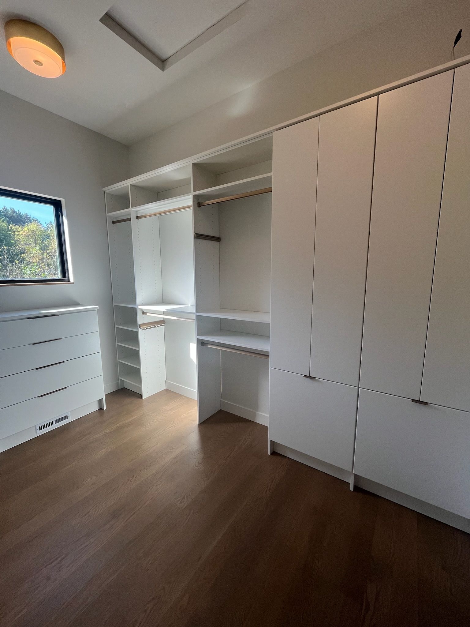 Bright empty closet room with white built-in shelves, drawers, and sliding doors on wood flooring.