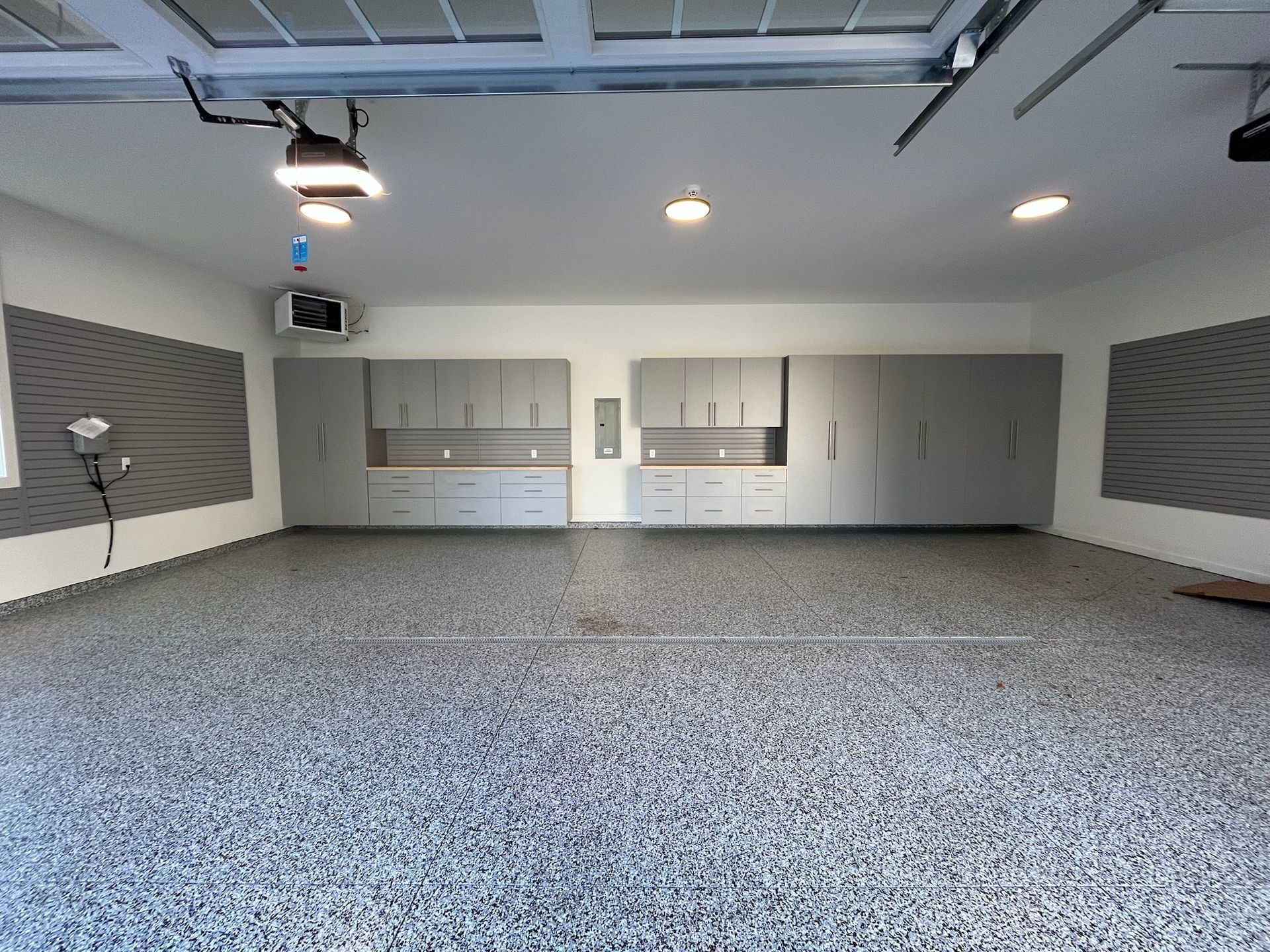 Empty garage with gray walls, cabinets, and a speckled floor, lit by overhead lights.