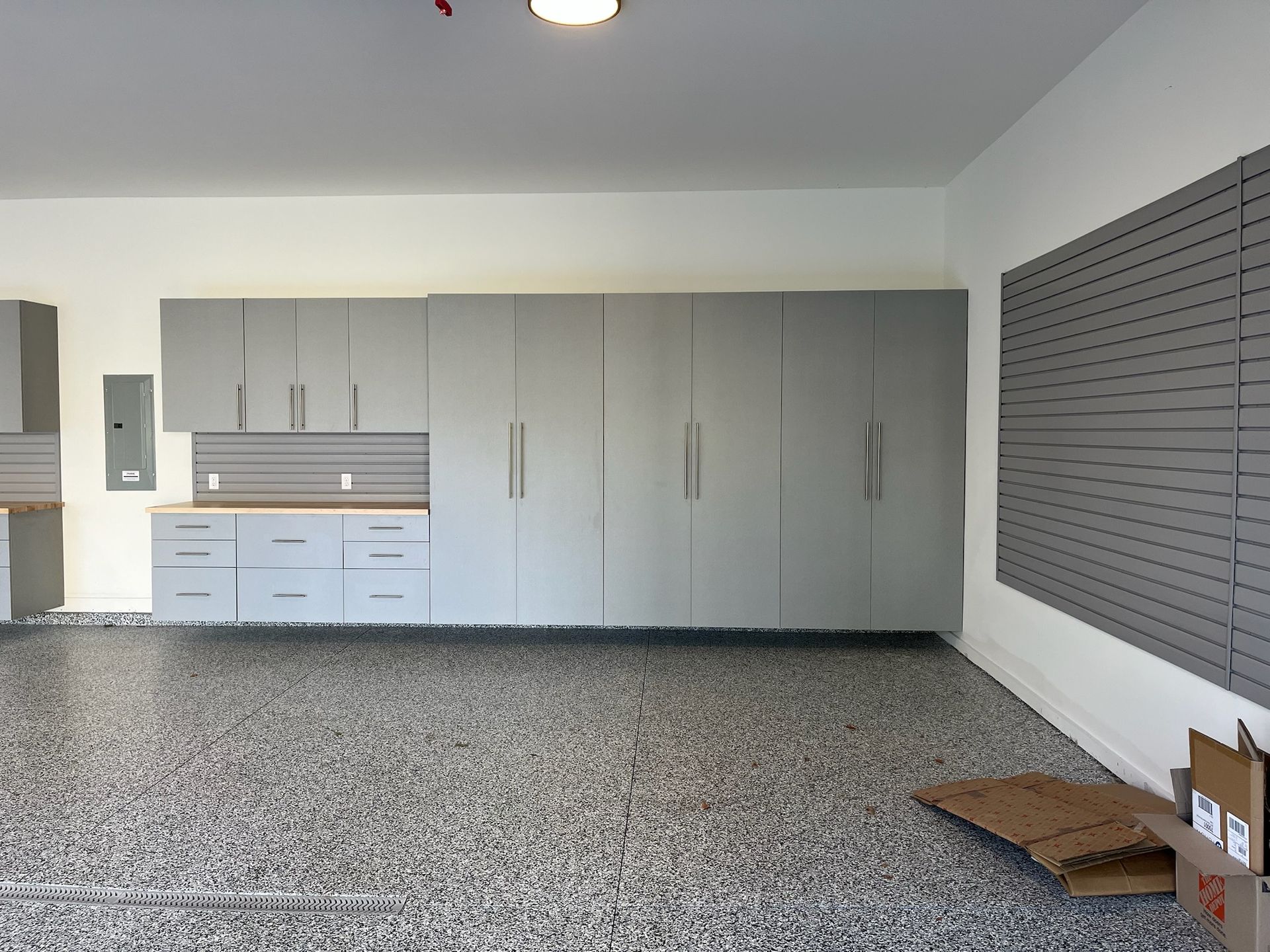 Empty garage with gray cabinets, speckled floor, and wall-mounted blinds.