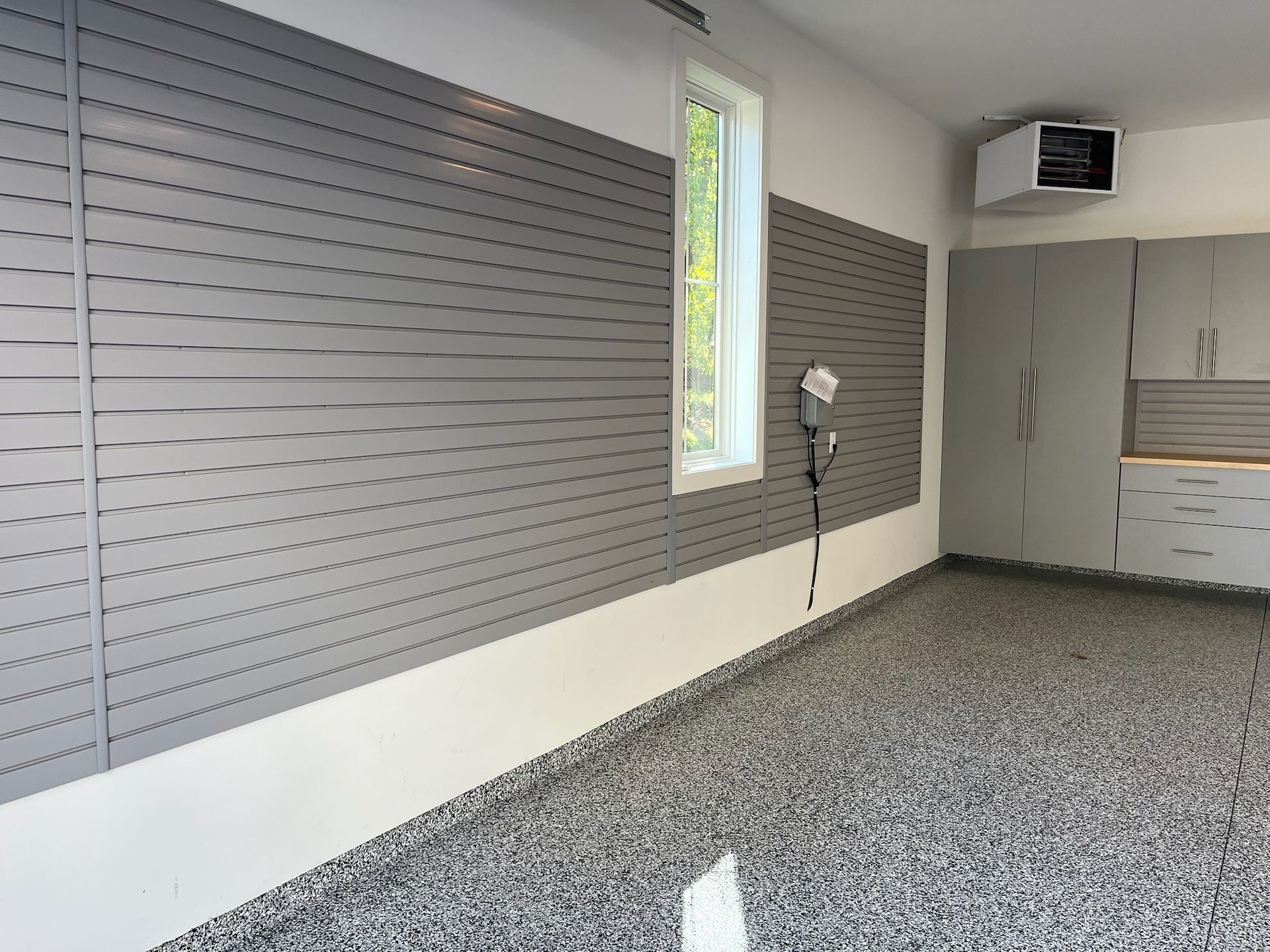 Empty music room with gray acoustic wall panels, a window, and a microphone stand on a speckled floor.