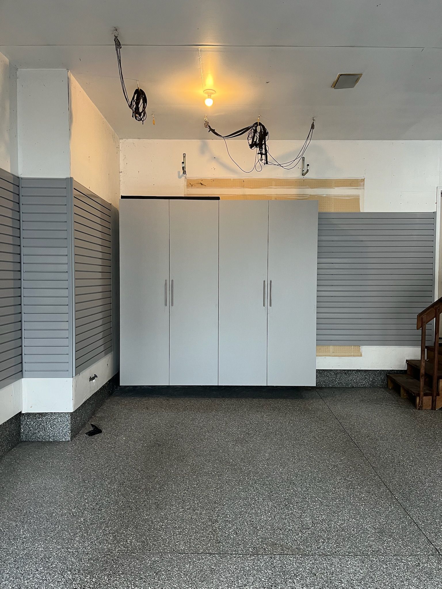 Garage interior with gray storage cabinets, ceiling lights, and slatwall panels on both sides.