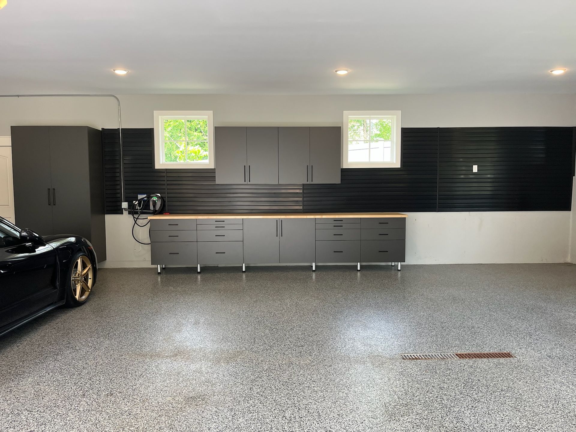 Spacious garage with black and gray cabinets, two windows, and a speckled epoxy floor; car partially visible on left