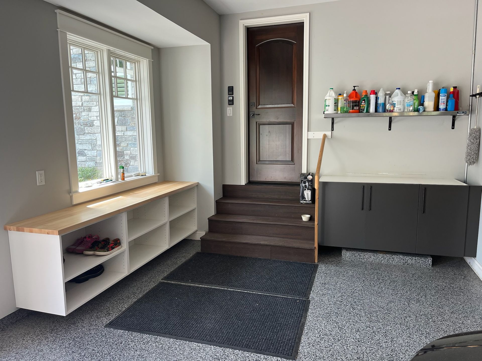 Garage mudroom with bench, stairs, cabinet, and wall shelf with bottles