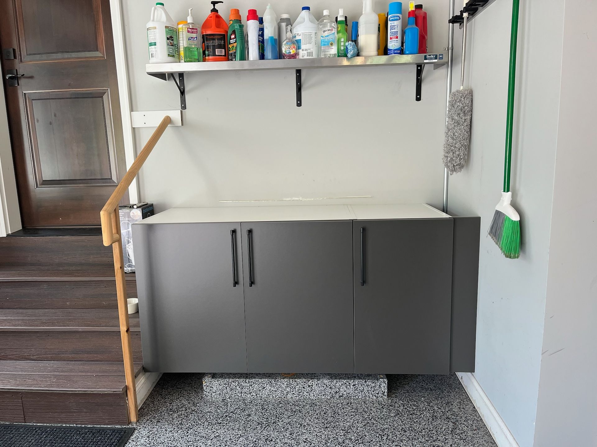 Garage storage cabinet with countertop and shelves, next to stairs, holding cleaning supplies.