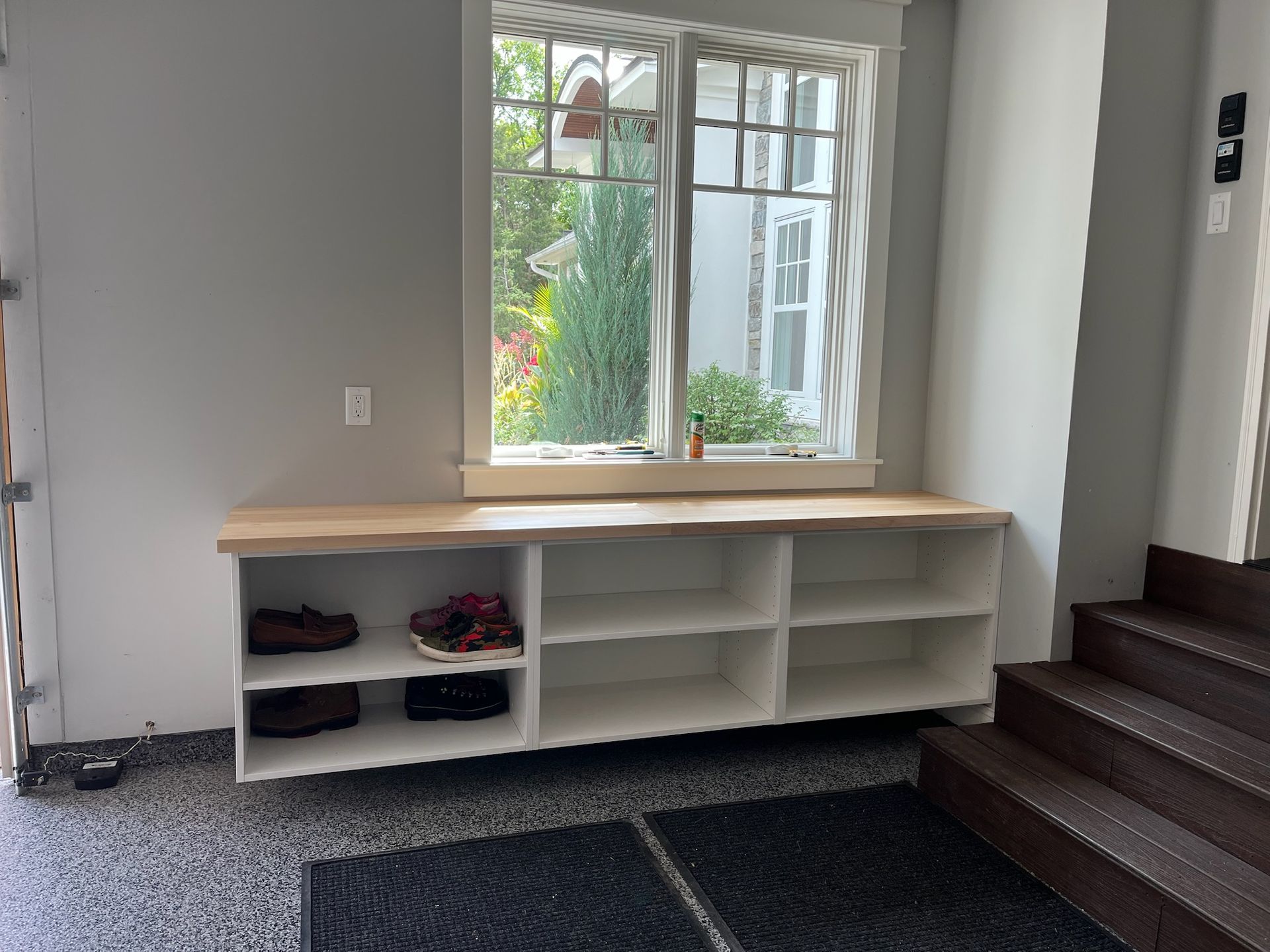 White entryway bench with cubbies and shoes beneath a window beside carpeted stairs