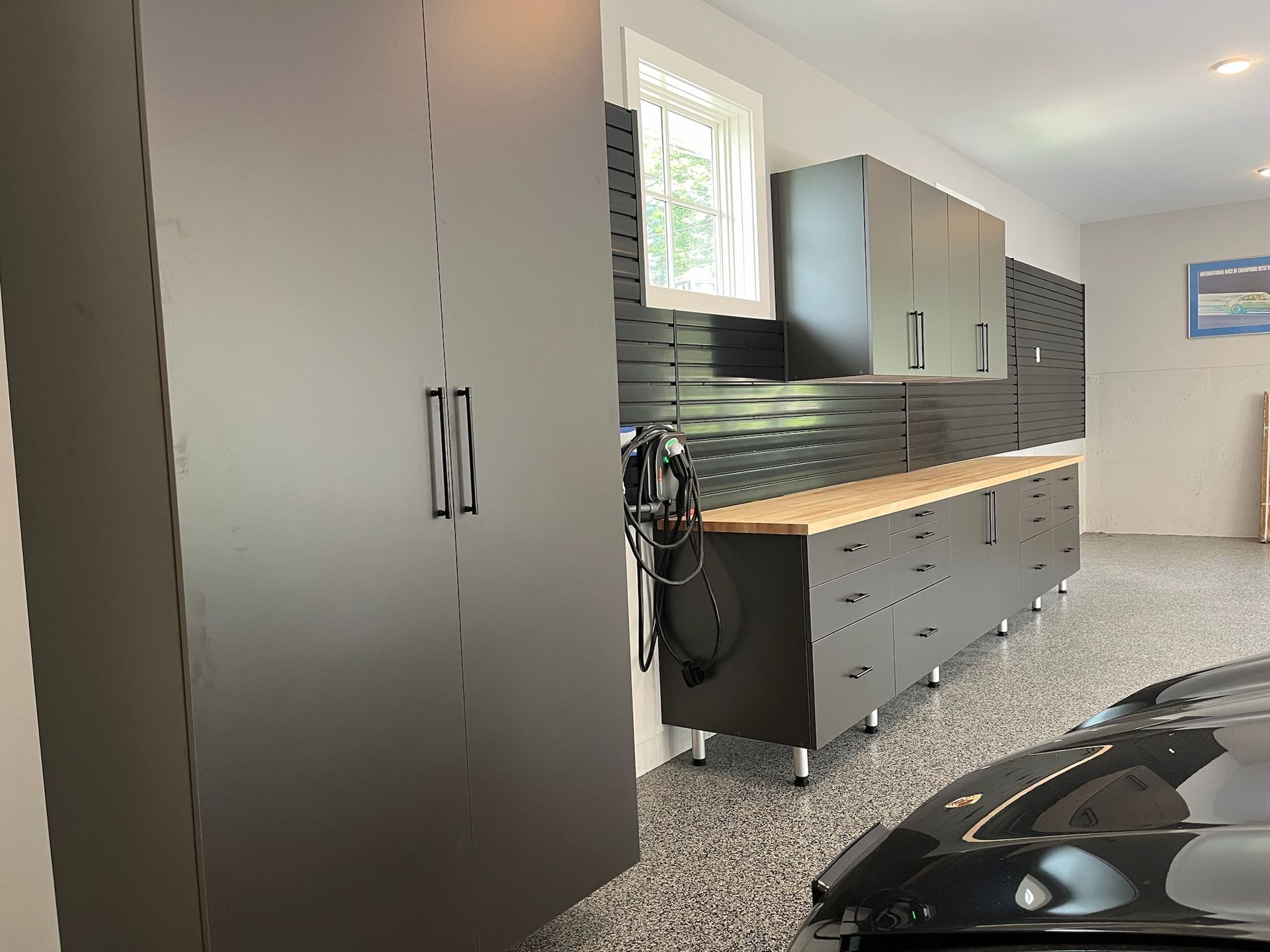 Garage interior with dark cabinets, workbench, and a black car in the foreground.