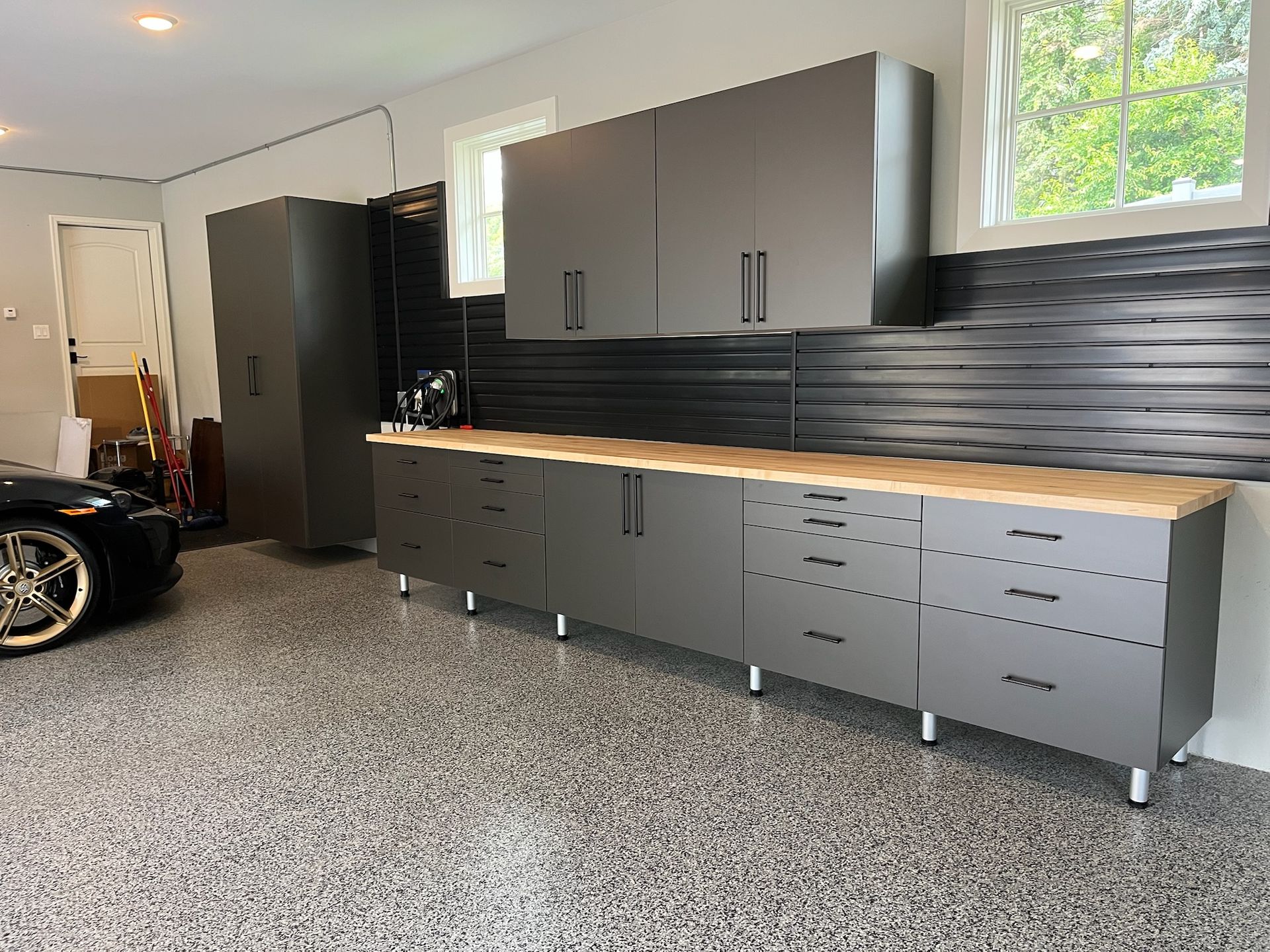Modern gray garage with cabinets, wood countertop, black backsplash, and a glimpse of a car on the left
