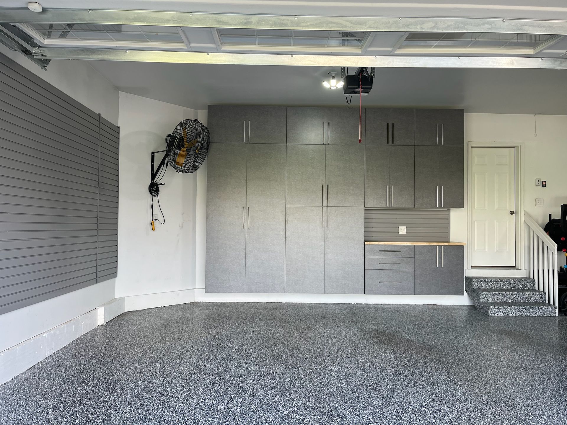 Empty garage with gray cabinets, wall fan, and a carpeted floor.