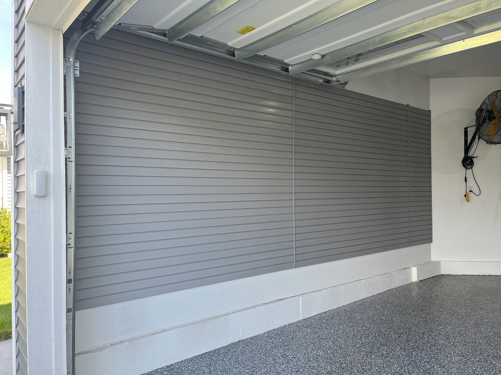 Gray slatwall storage panel inside an empty garage with gravel flooring
