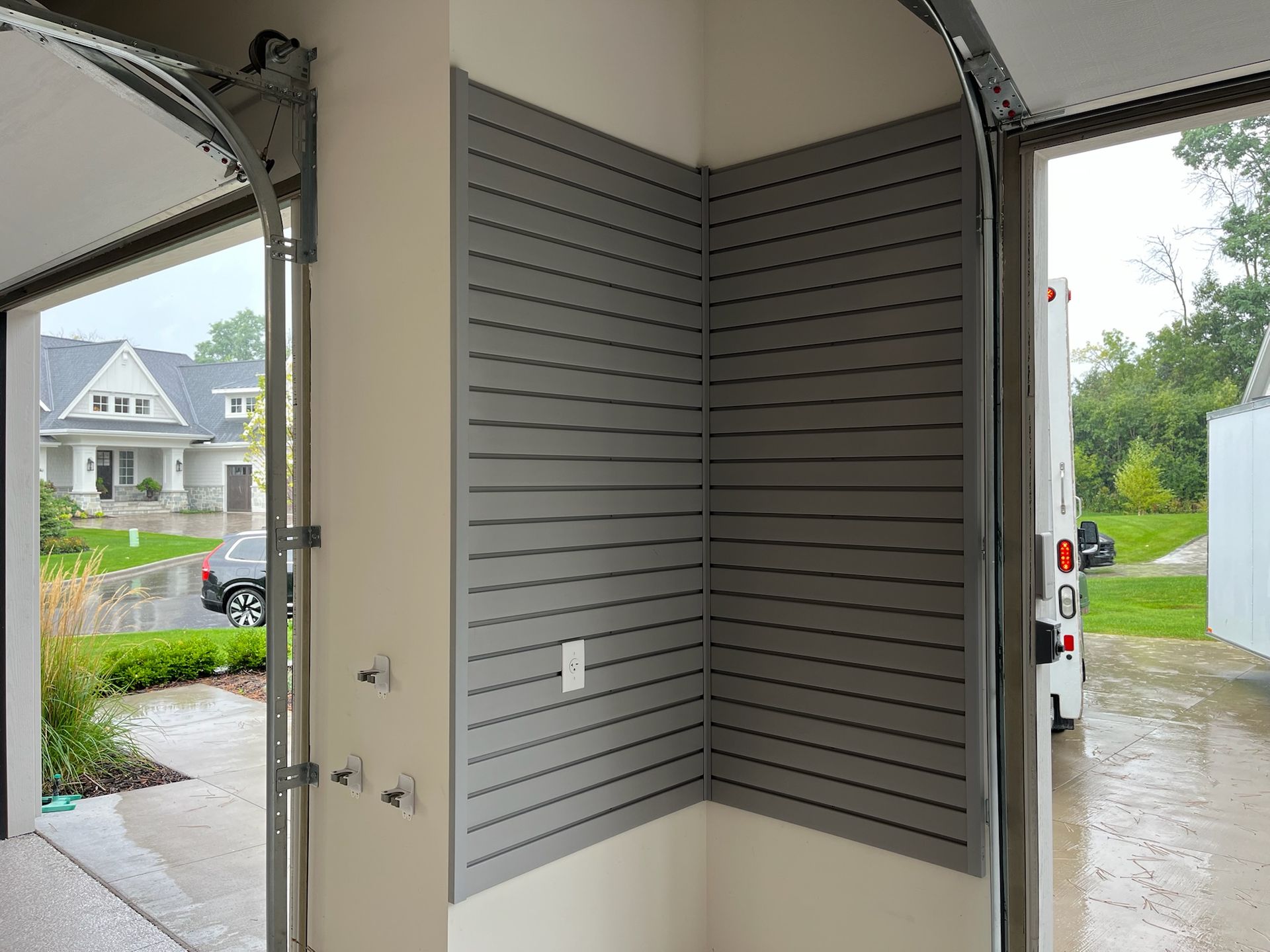 Empty garage with gray slat walls and open door to a wet driveway and suburban street.