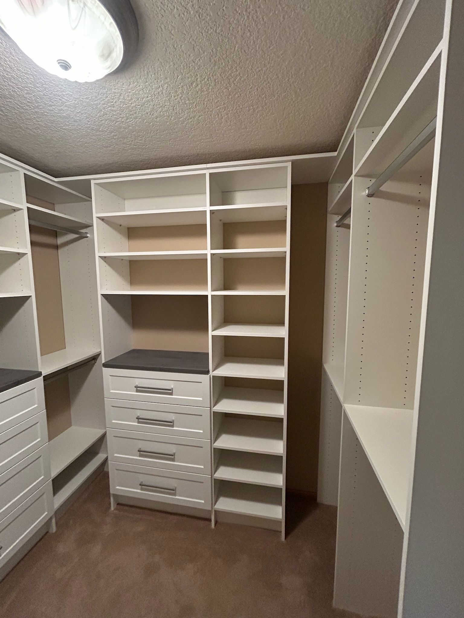 Walk-in closet with white built-in shelves, drawers, and hanging rods under a ceiling light.