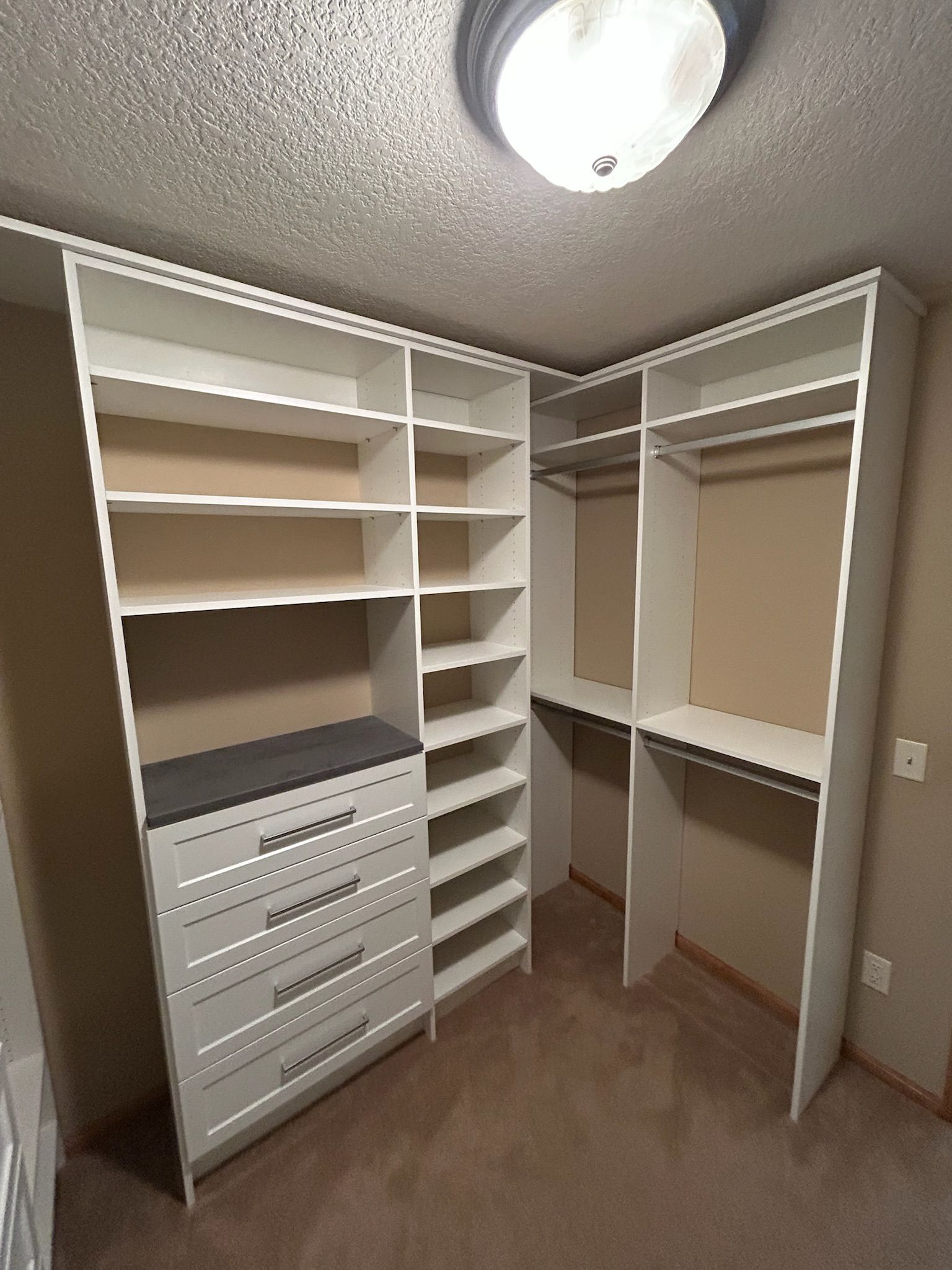 Walk-in closet with white built-in shelves, drawers, hanging rods, and beige carpet under ceiling light