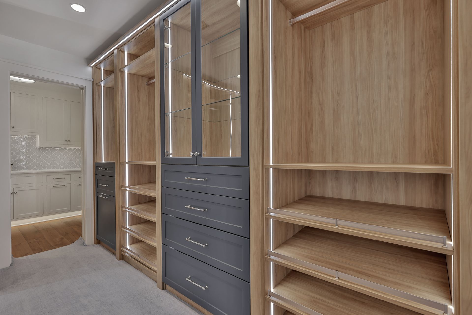 Walk-in closet with light wood shelving, hanging rails, and dark drawers under bright lighting