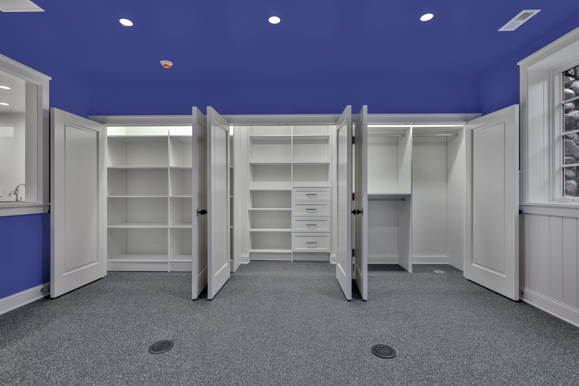 Empty white closet room with blue walls and carpeted floor, open shelving and hanging rods