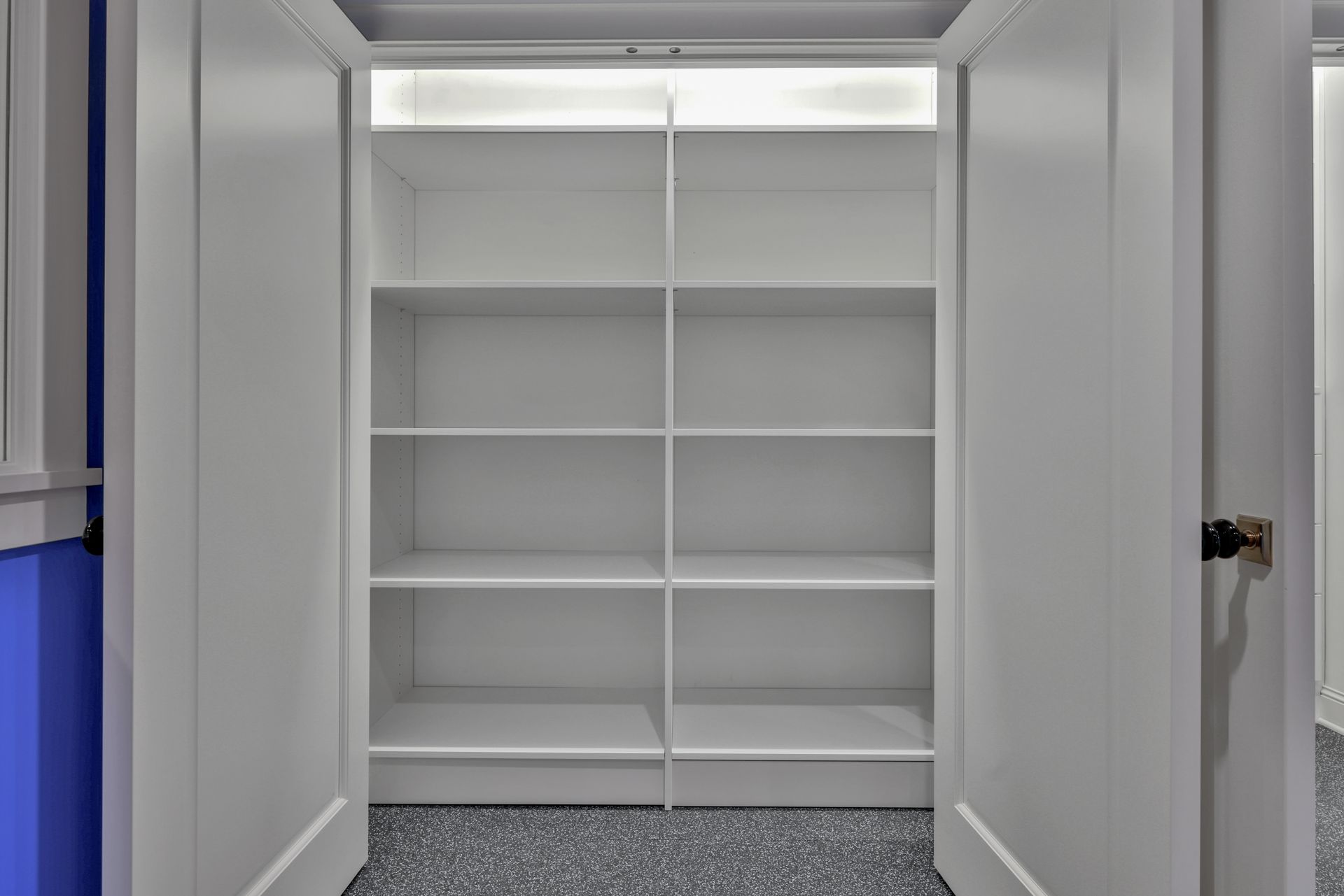 Empty white closet with built-in shelves and a dark carpeted floor